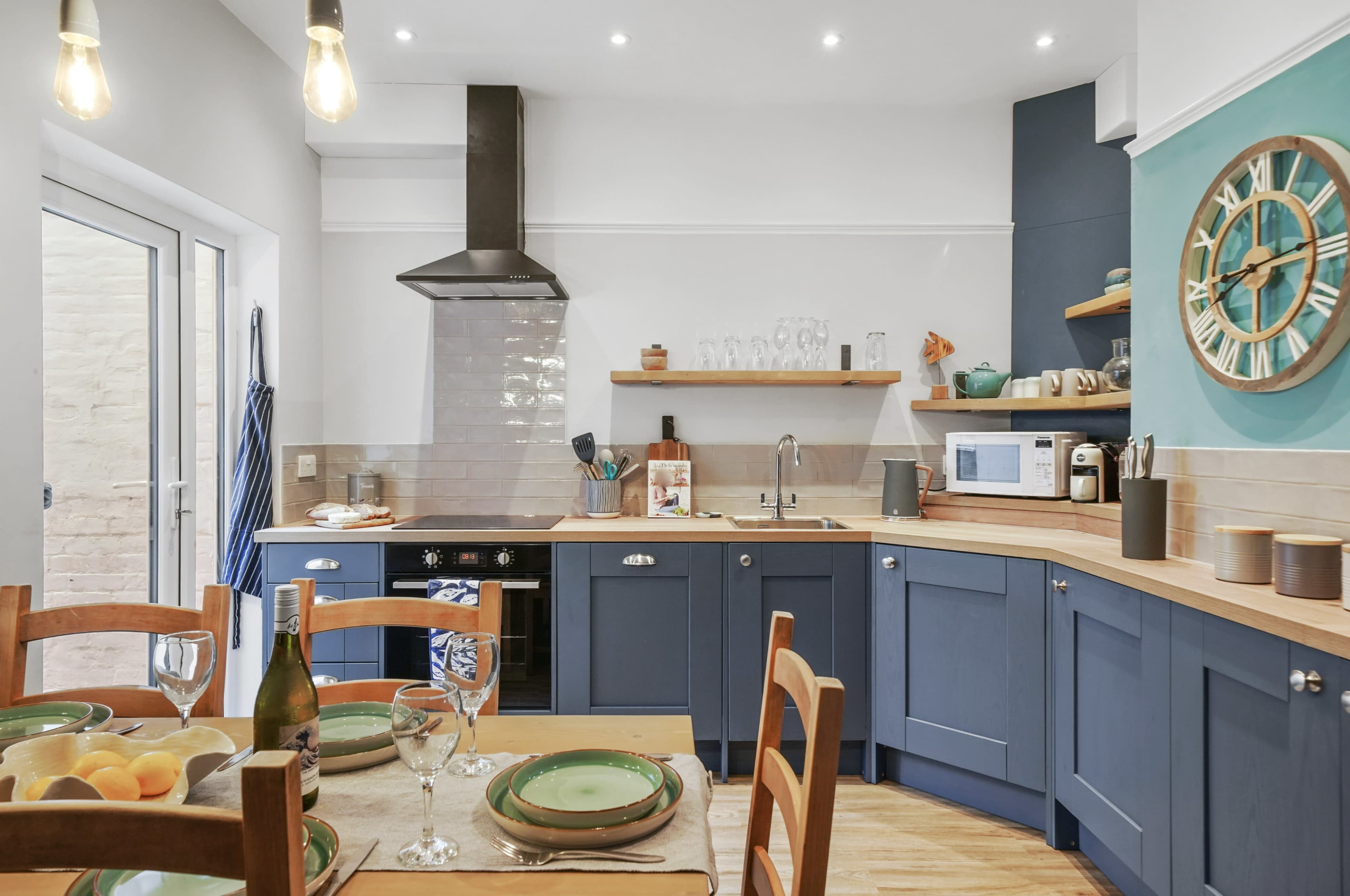A modern kitchen features blue cabinetry, wooden countertops, and an island, with a dining table set for a meal.