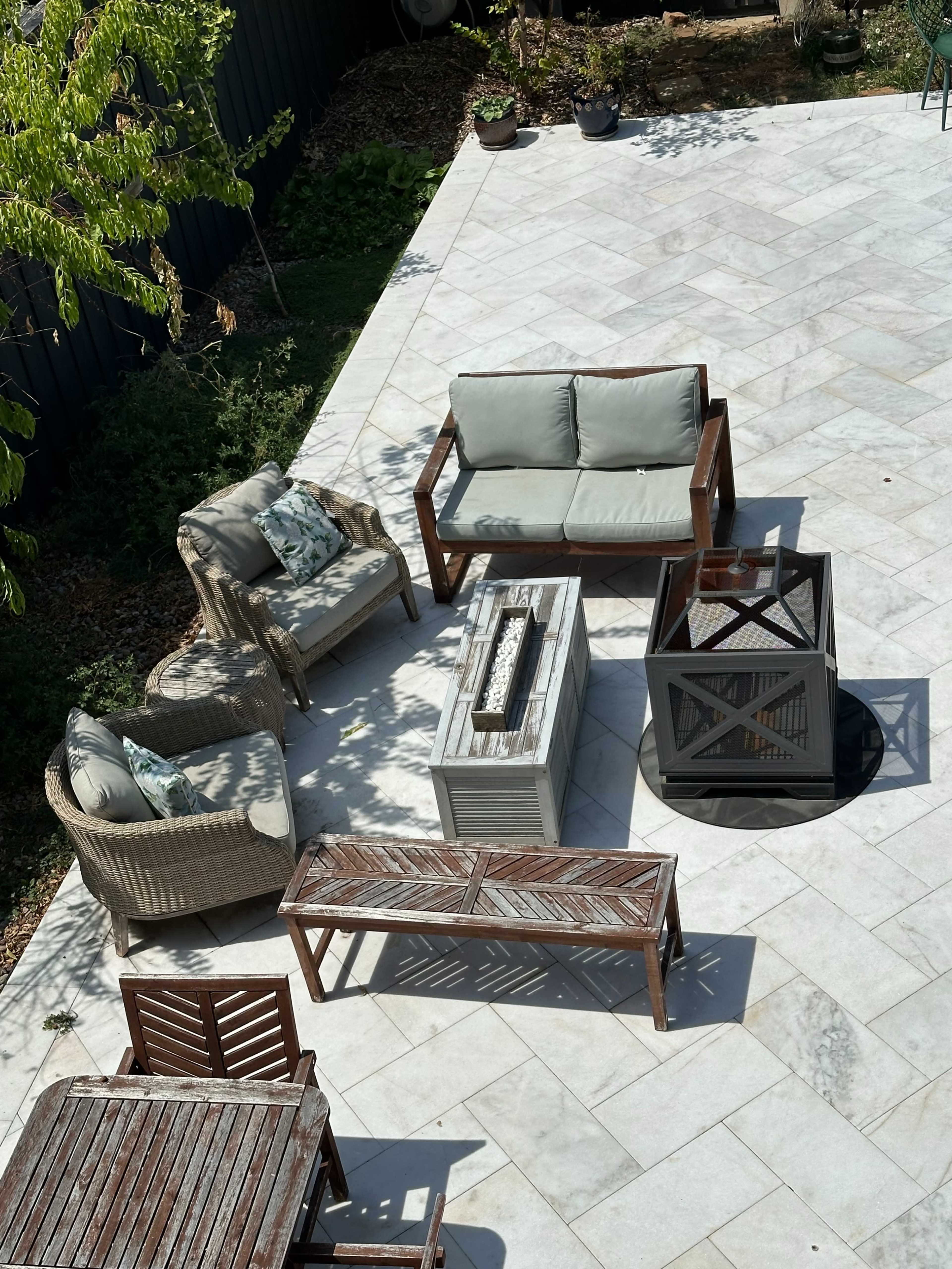 An outdoor seating area features a mix of wicker and wooden furniture arranged around a central fire pit on a stone patio.
