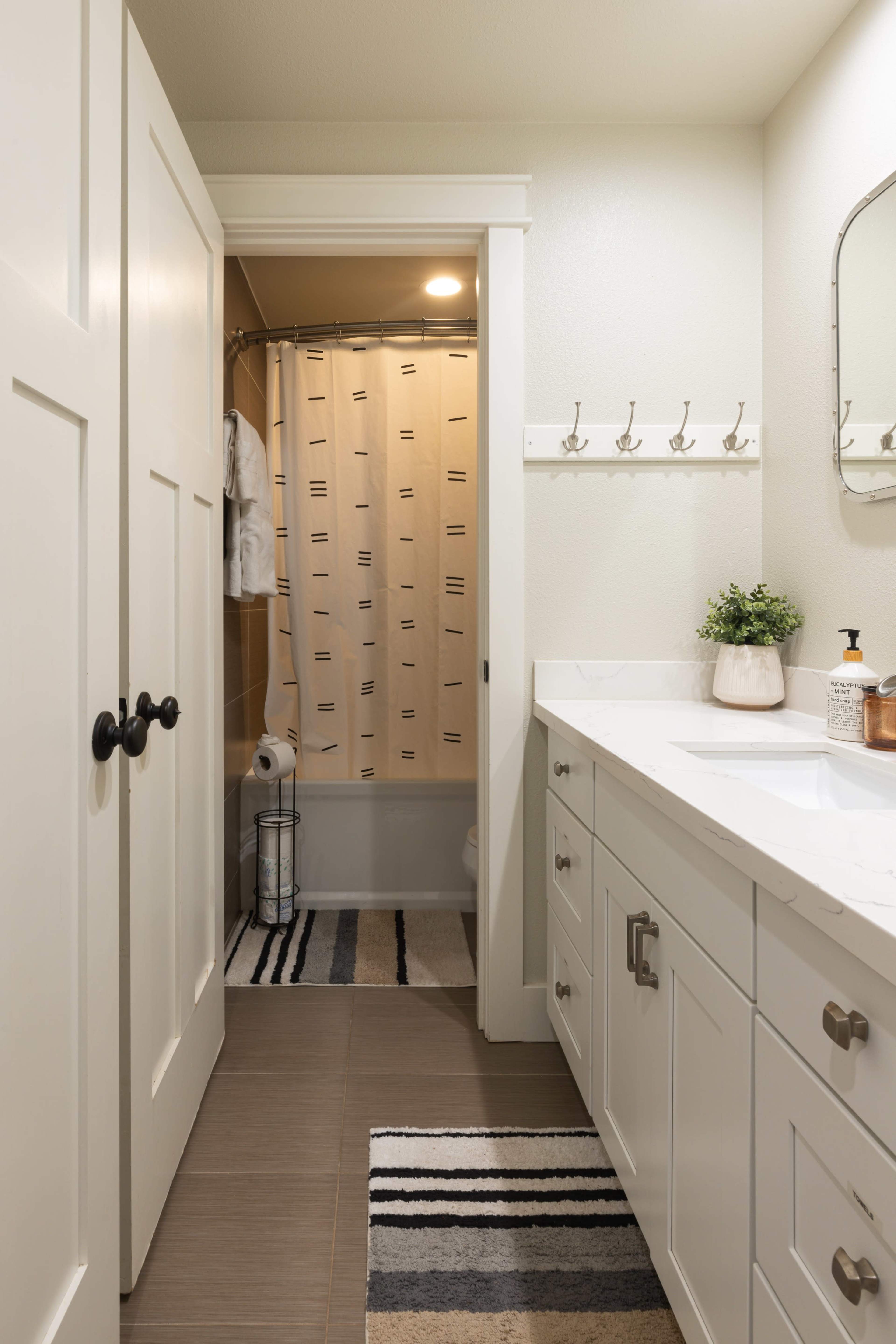 A well-lit bathroom features a shower area with a curtain, a vanity with a sink, and a door leading to an adjacent space.