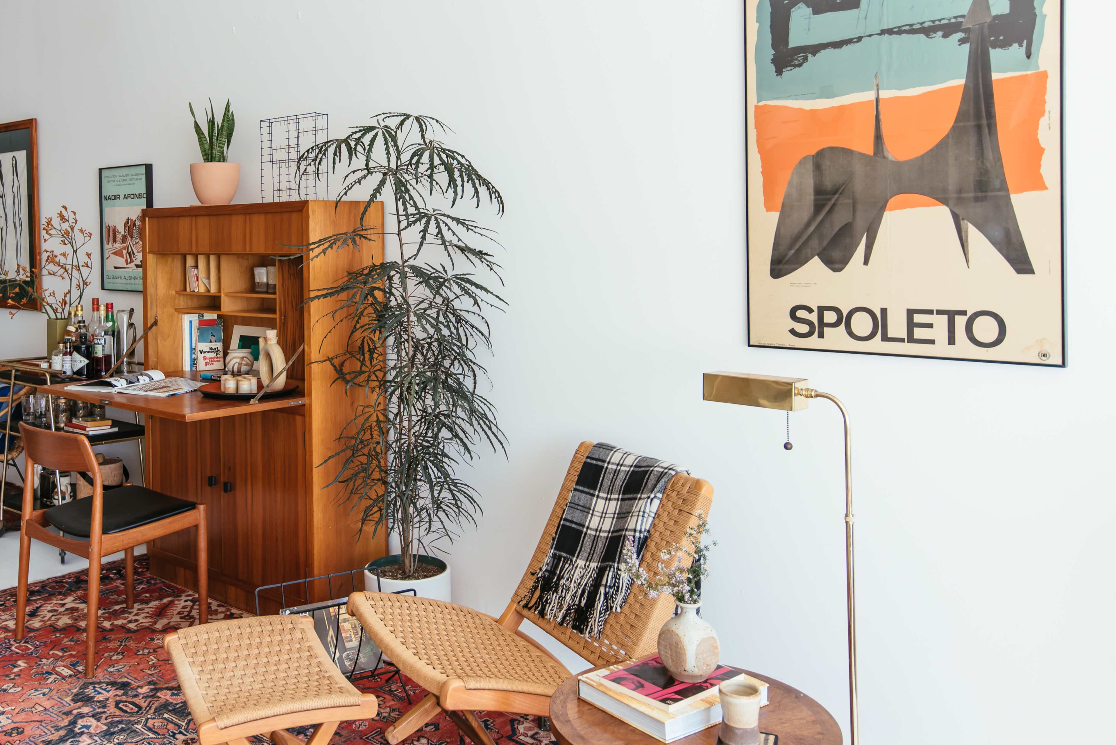 A well-furnished living room corner with a wooden desk, a modern poster on the wall, a potted plant, and a cozy seating area.