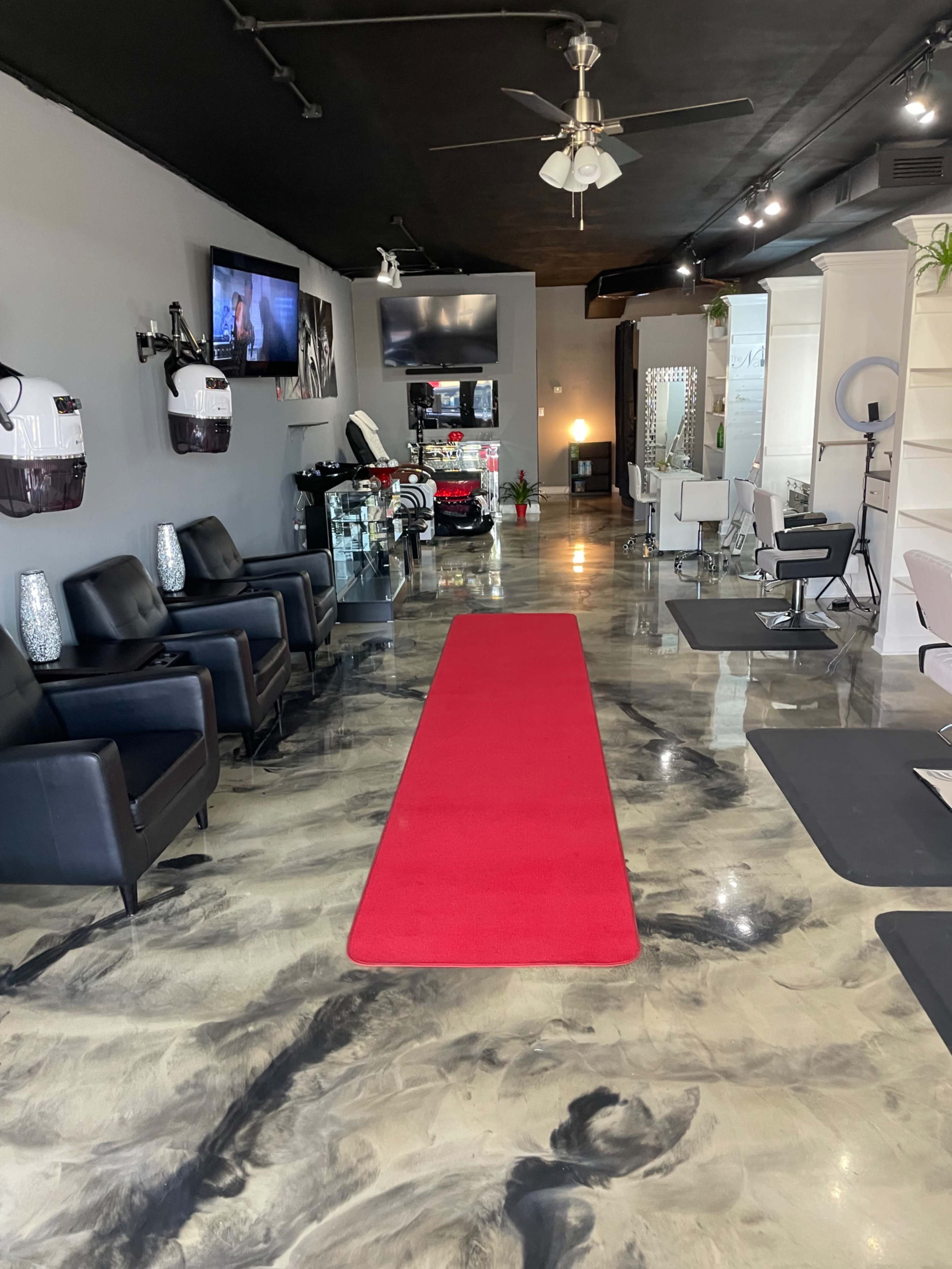 A beauty salon interior featuring a red carpet, black leather chairs, and sleek furnishings under a modern lighting setup.