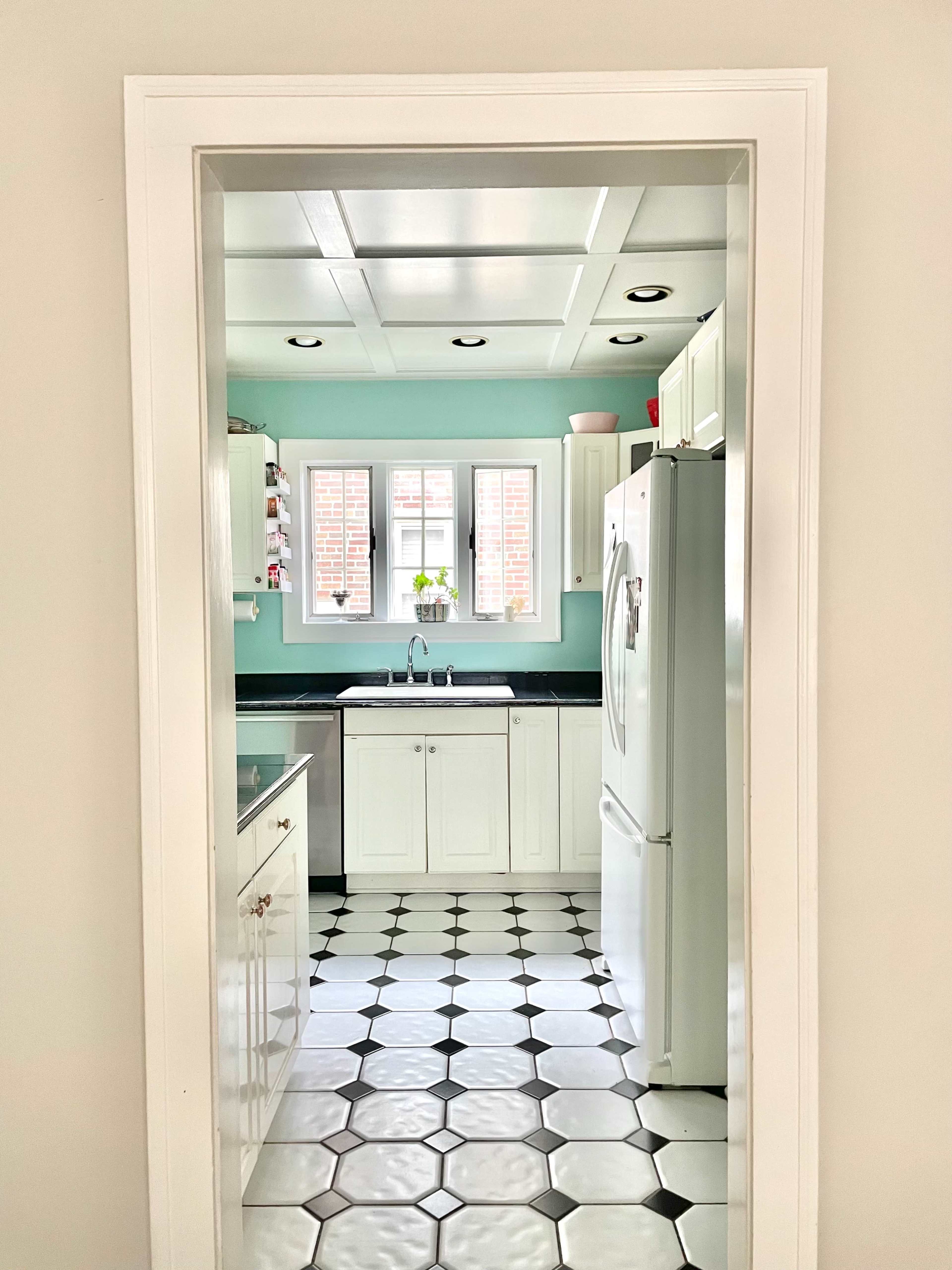 A view of a kitchen with white cabinets, a black countertop, and a checkered black and white tile floor, visible through an archway.