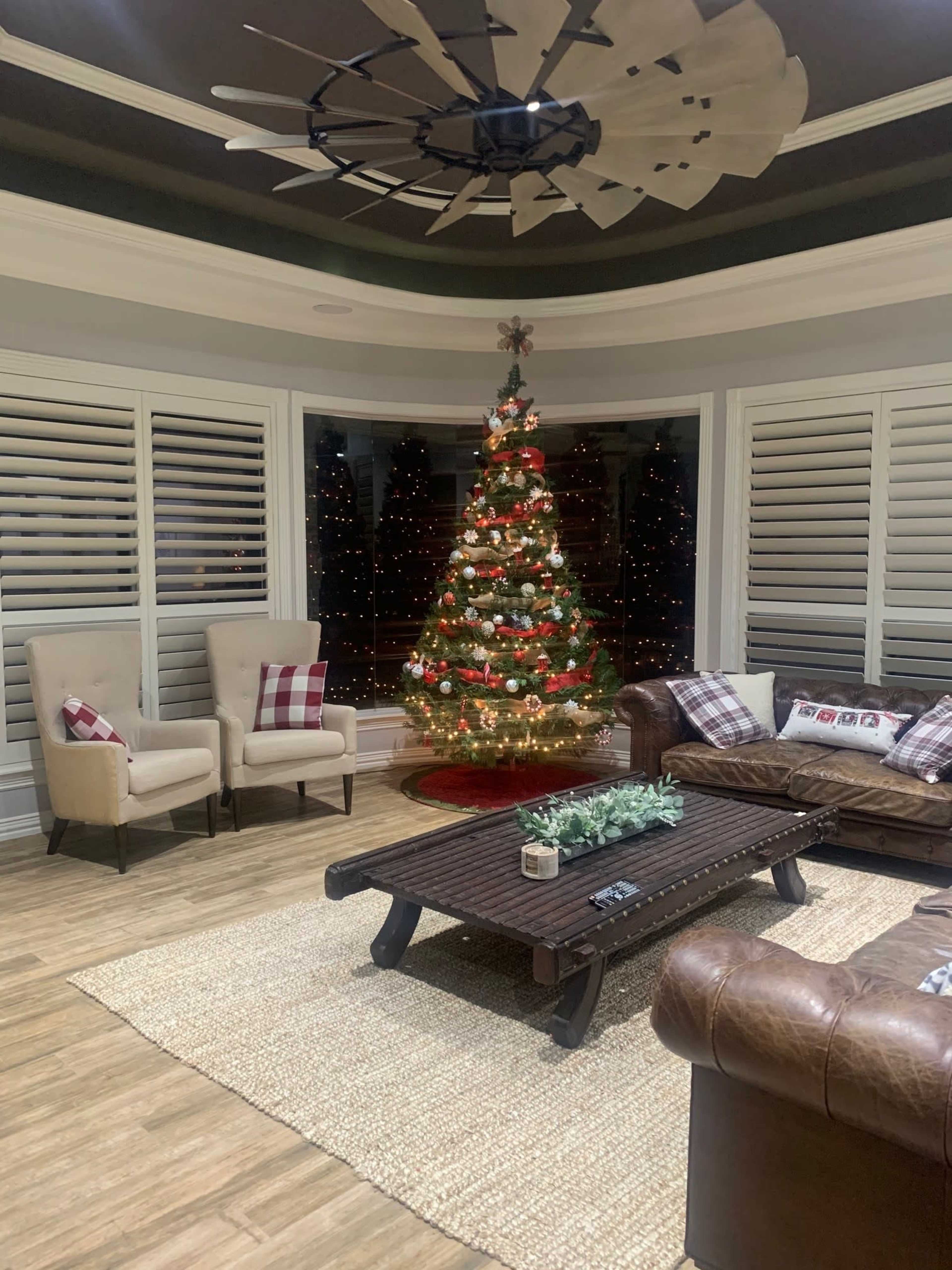 A living room with a Christmas tree adorned with lights and decorations, surrounded by comfortable seating and a coffee table on a rug.