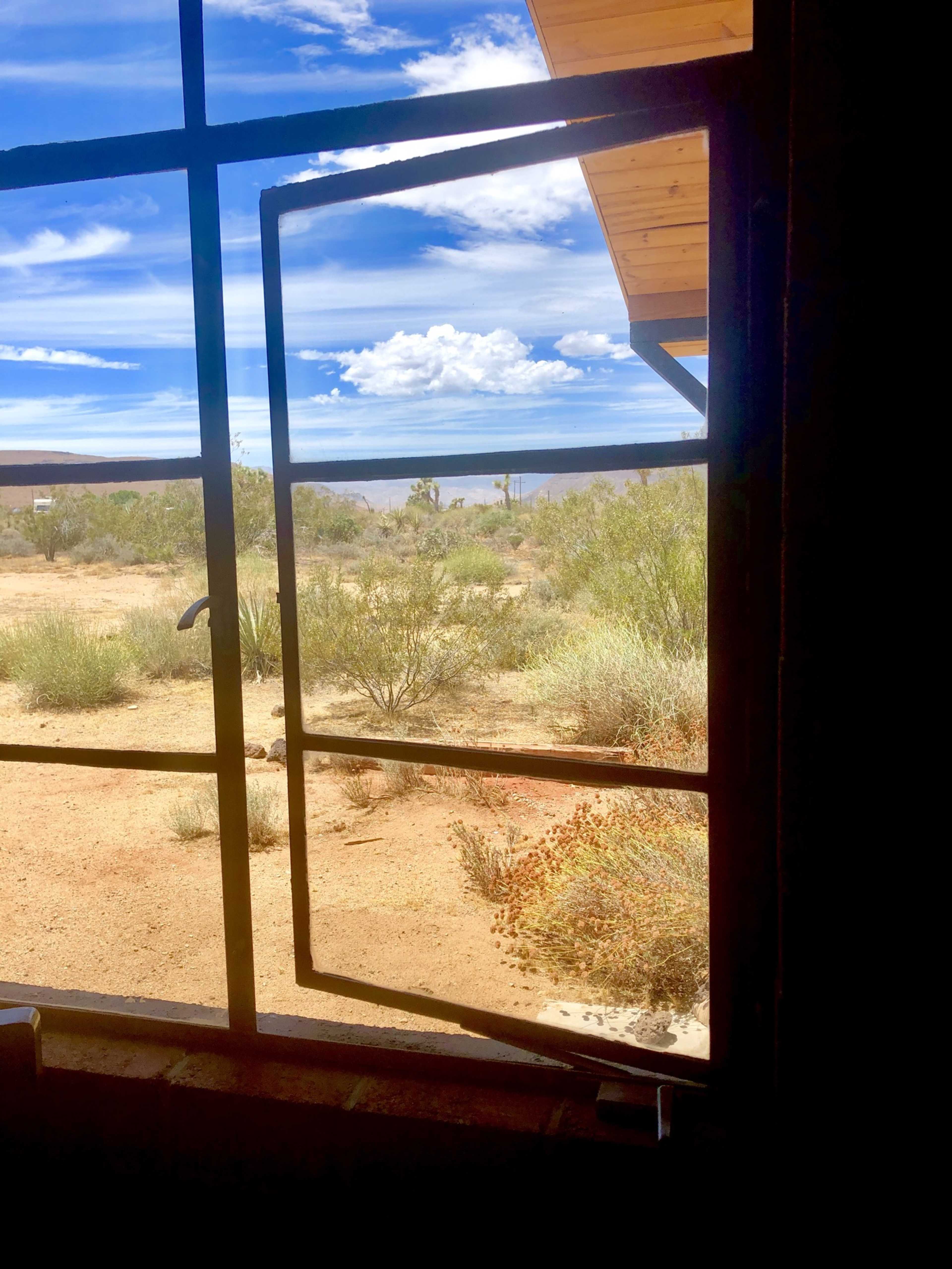 An open window with a metal frame overlooking a desert landscape with sparse vegetation and blue skies.
