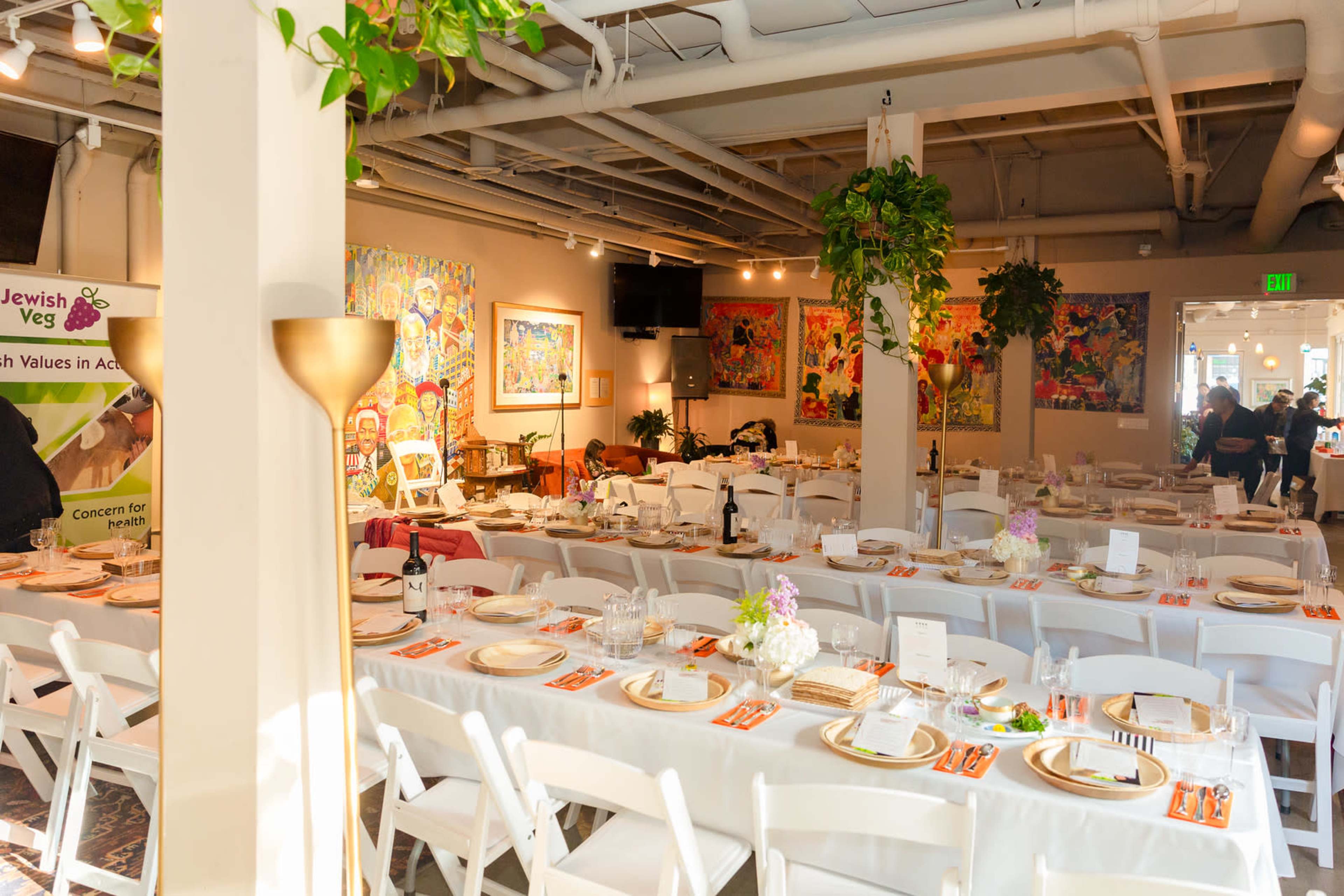 The image shows a dining area arranged with long tables set for a meal, decorated with flowers and colorful artwork on the walls.