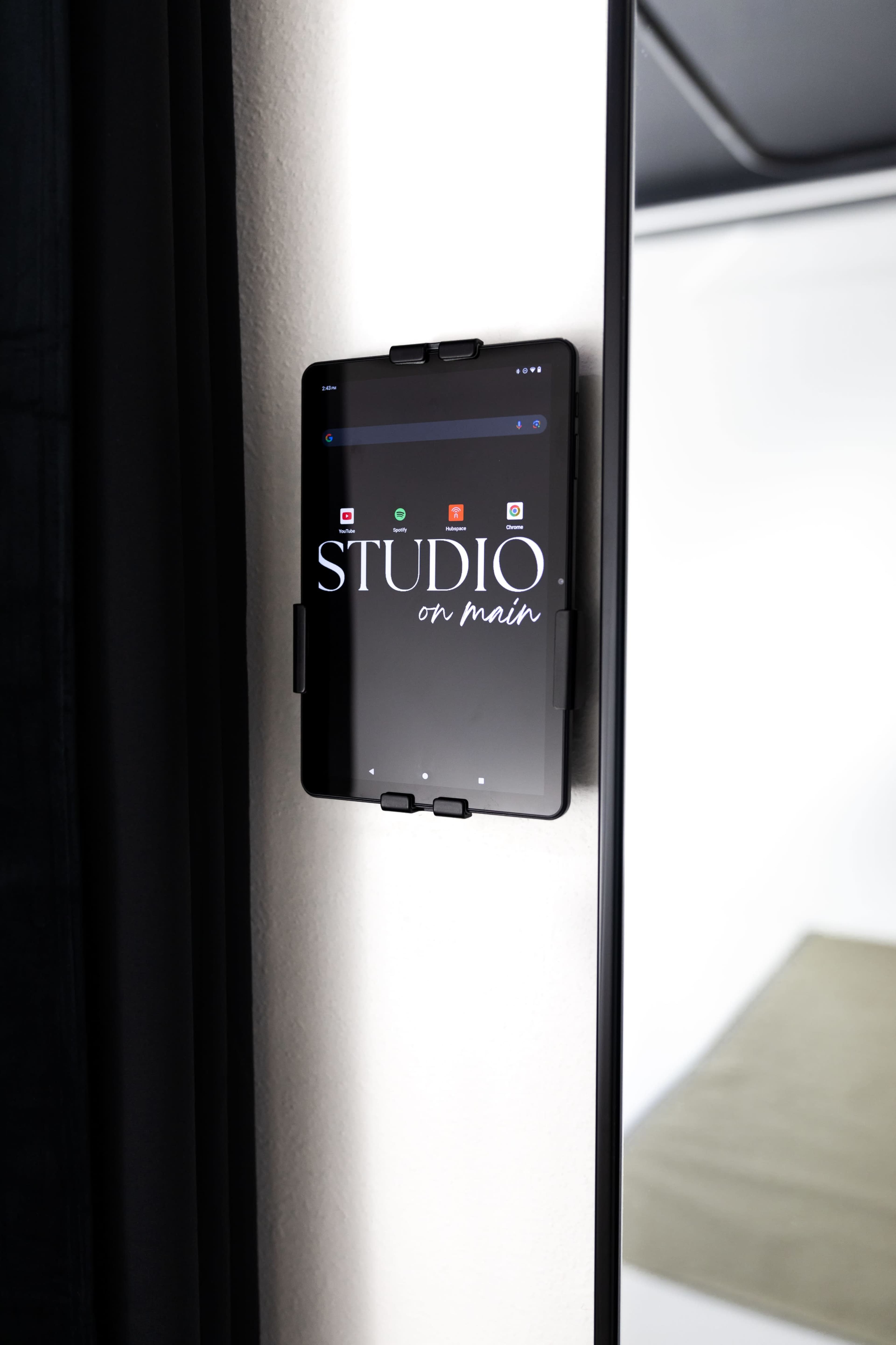 A tablet displaying the text "STUDIO on main" is mounted on a wall beside a black curtain.
