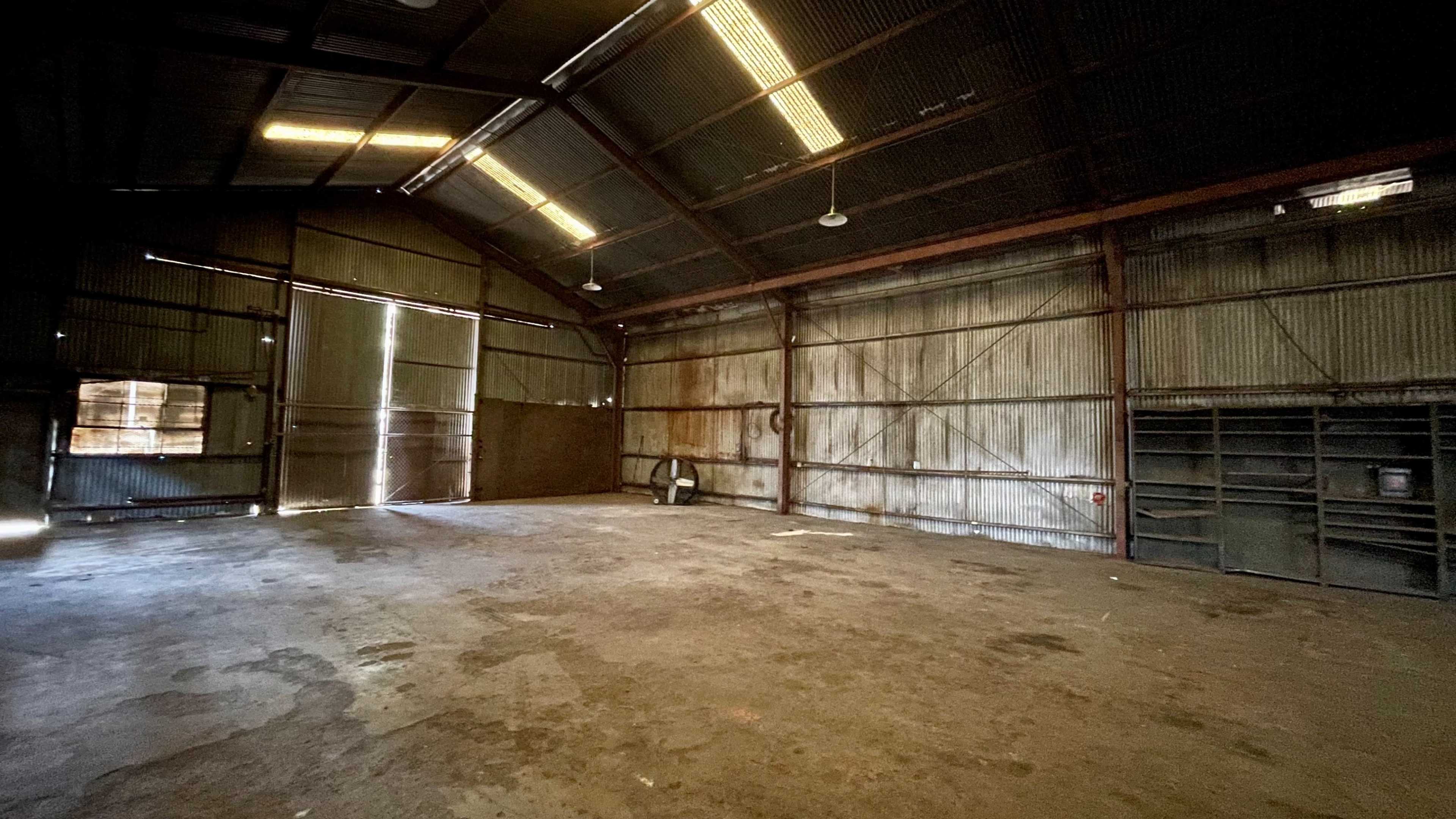 An empty industrial shed with metal walls, a high ceiling, and a large open door on one side.