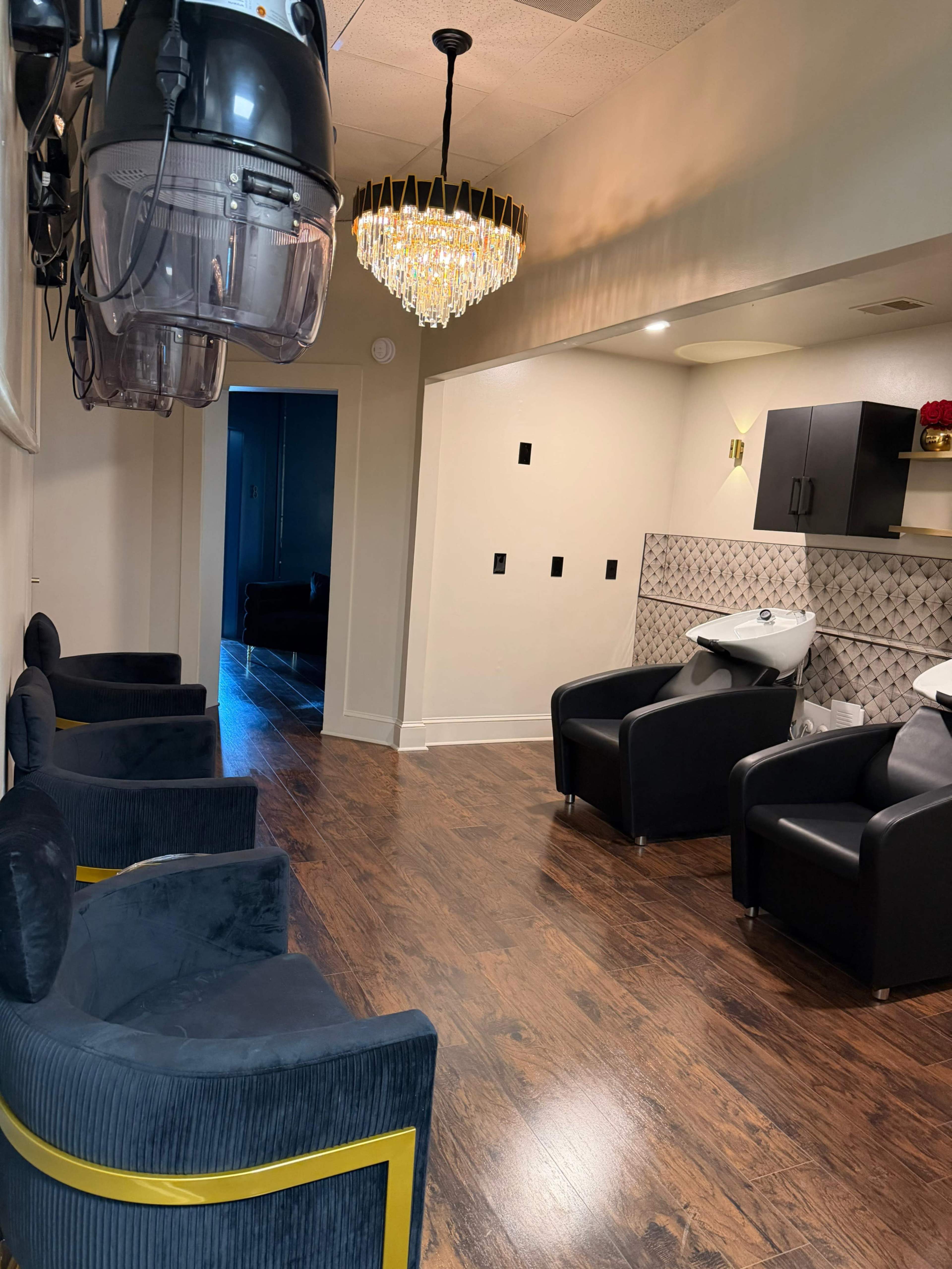 The image shows a hair salon interior with several black chairs, a chandelier overhead, and hair washing stations along the wall.
