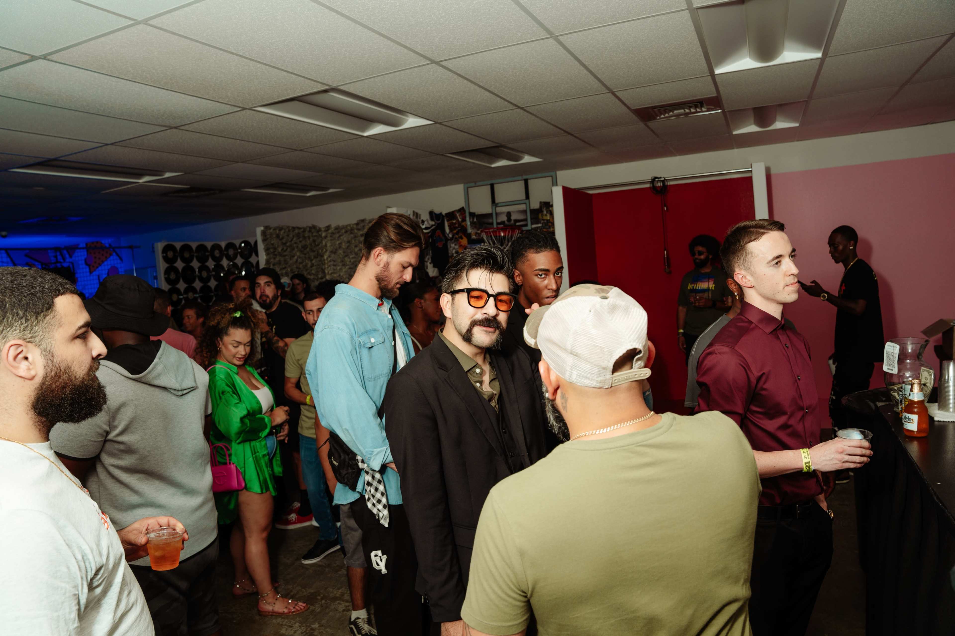 A crowd of people mingle in a brightly lit room filled with music equipment and colorful decorations.