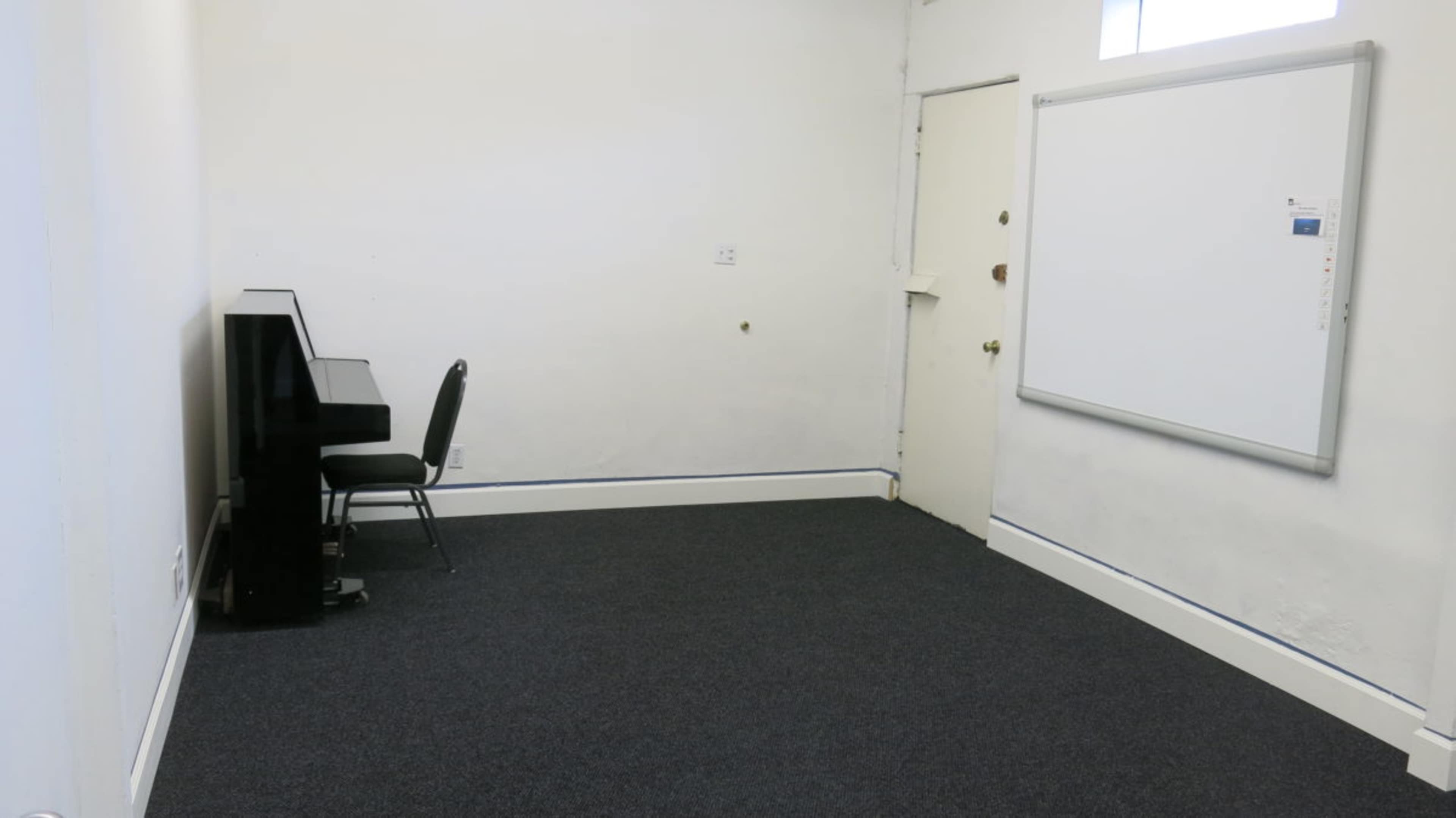 The image shows a sparsely furnished room with a piano, a chair, and a whiteboard near a door.