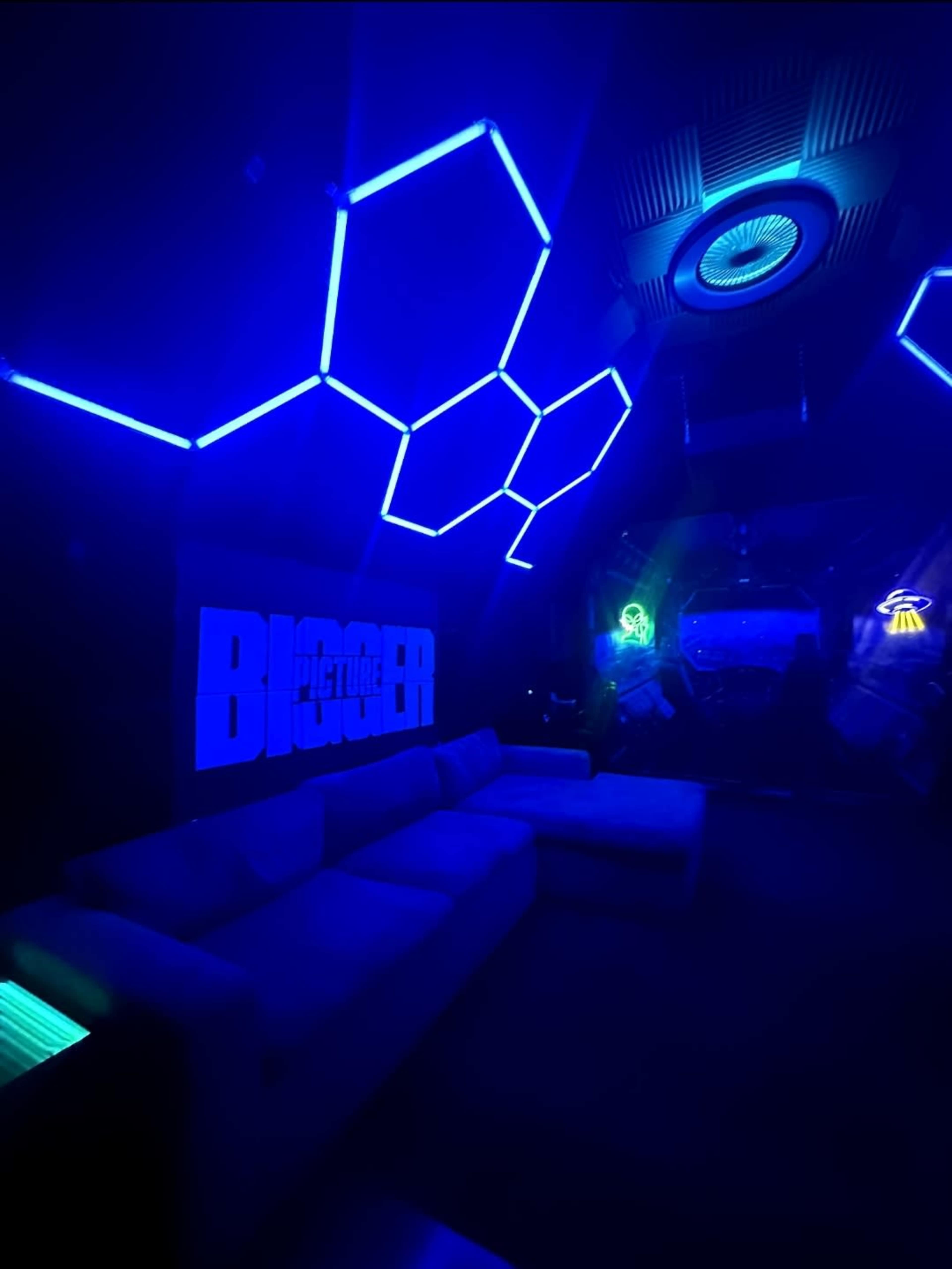 The image shows a dark room with blue LED lighting in a hexagonal pattern and a large sectional sofa.