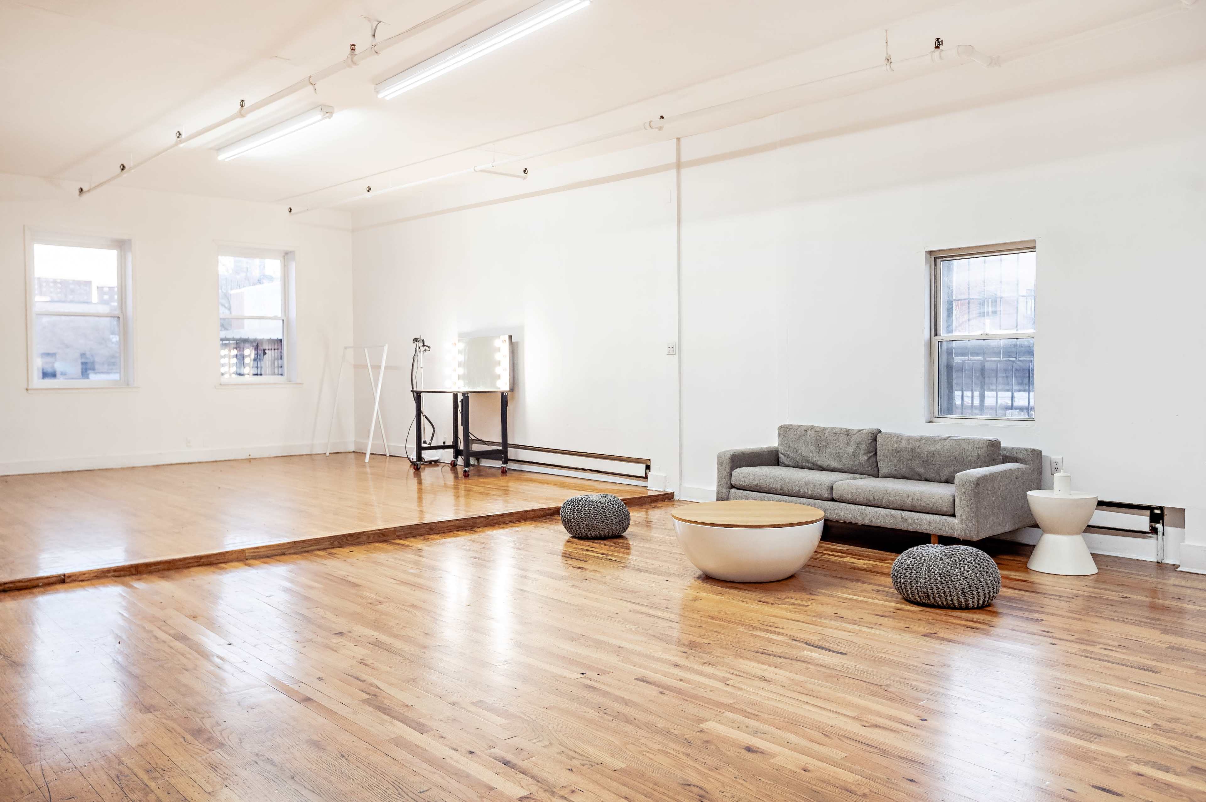 A spacious, minimalist room with hardwood floors, featuring a grey sofa, a round coffee table, and two decorative poufs.