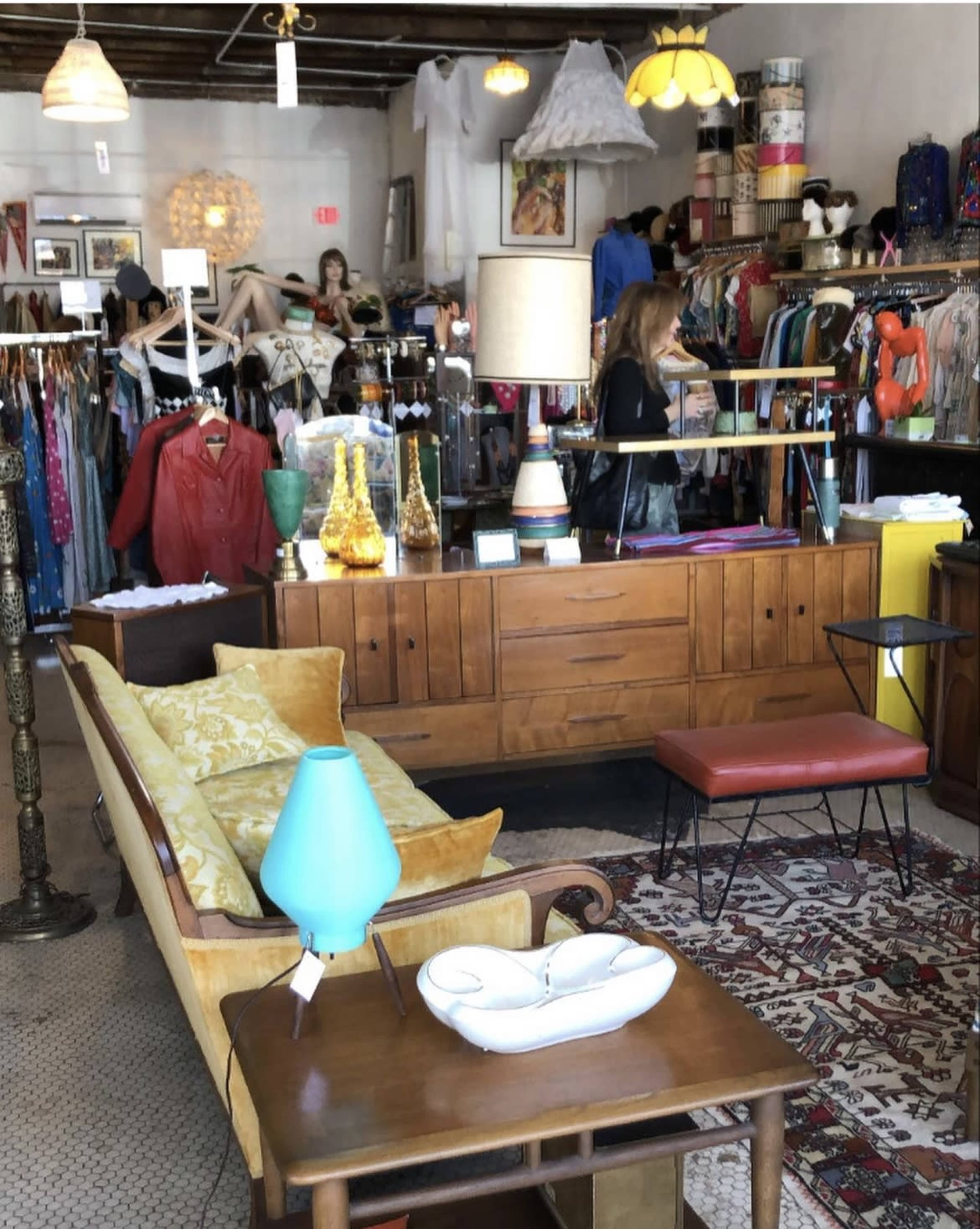 A vintage clothing store featuring a retro wooden counter, a yellow sofa, and various clothing items displayed on racks.
