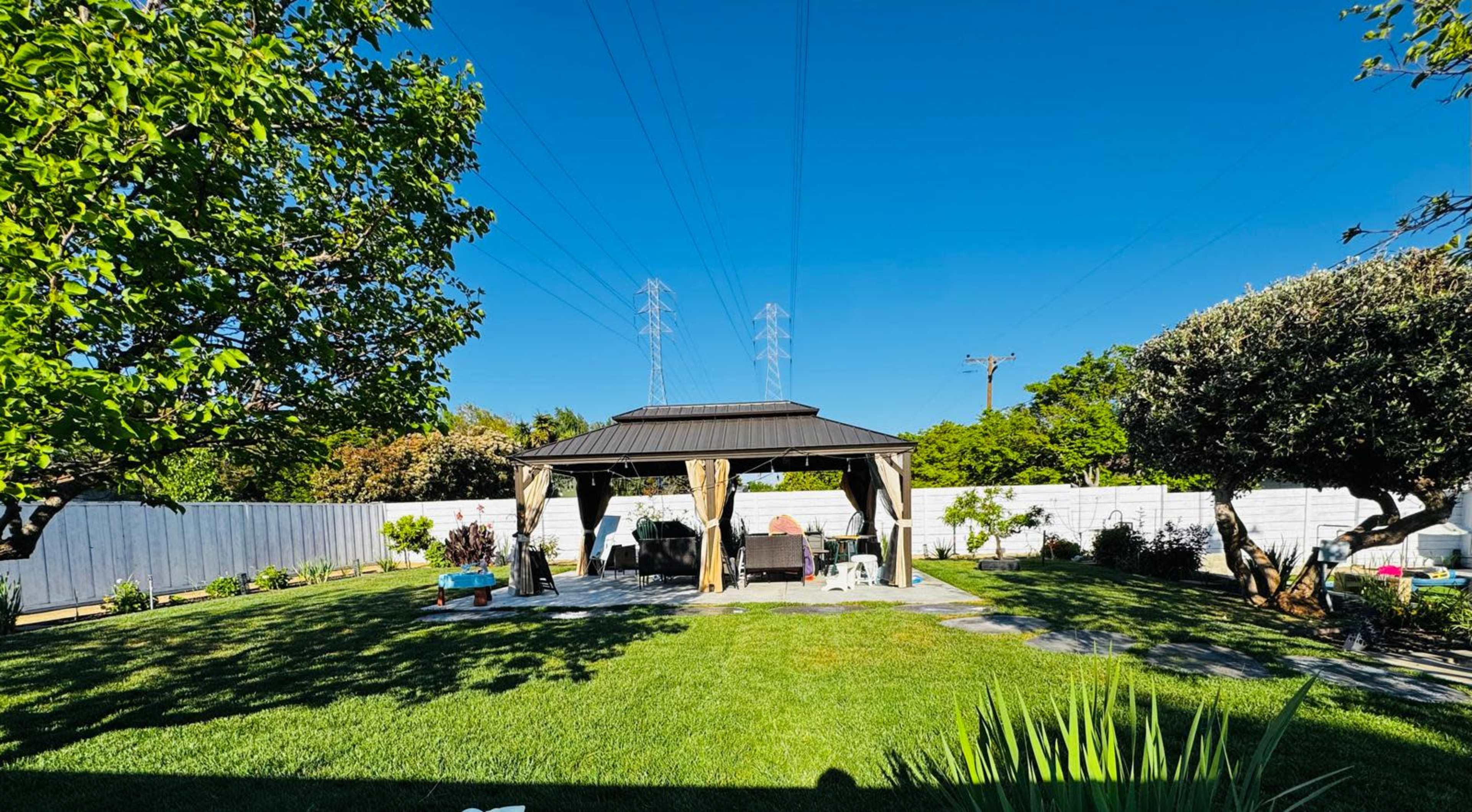 A backyard scene features a gazebo surrounded by grass and trees, with a clear blue sky above.
