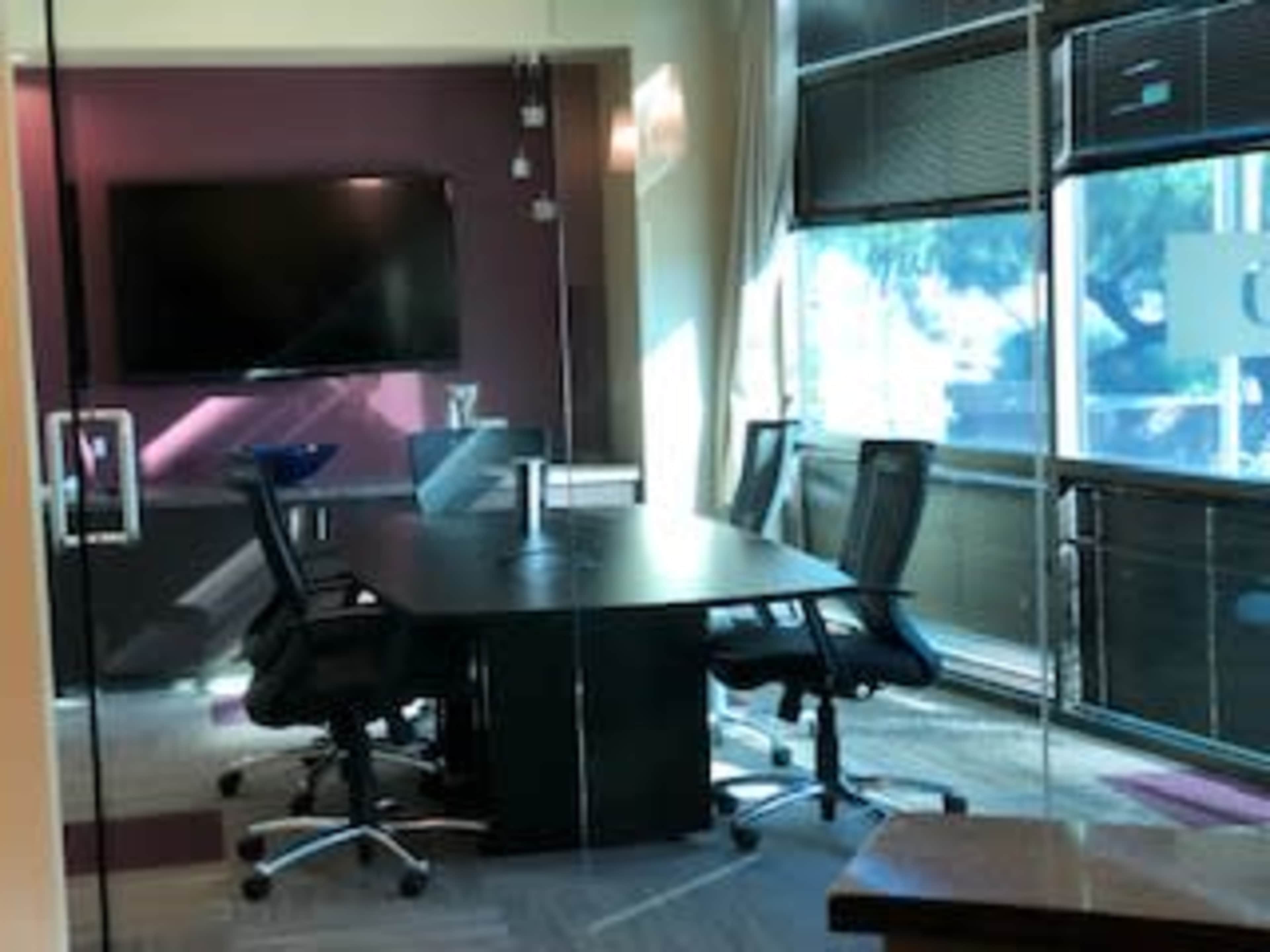 A modern conference room with a large table, four black chairs, and a wall-mounted screen.