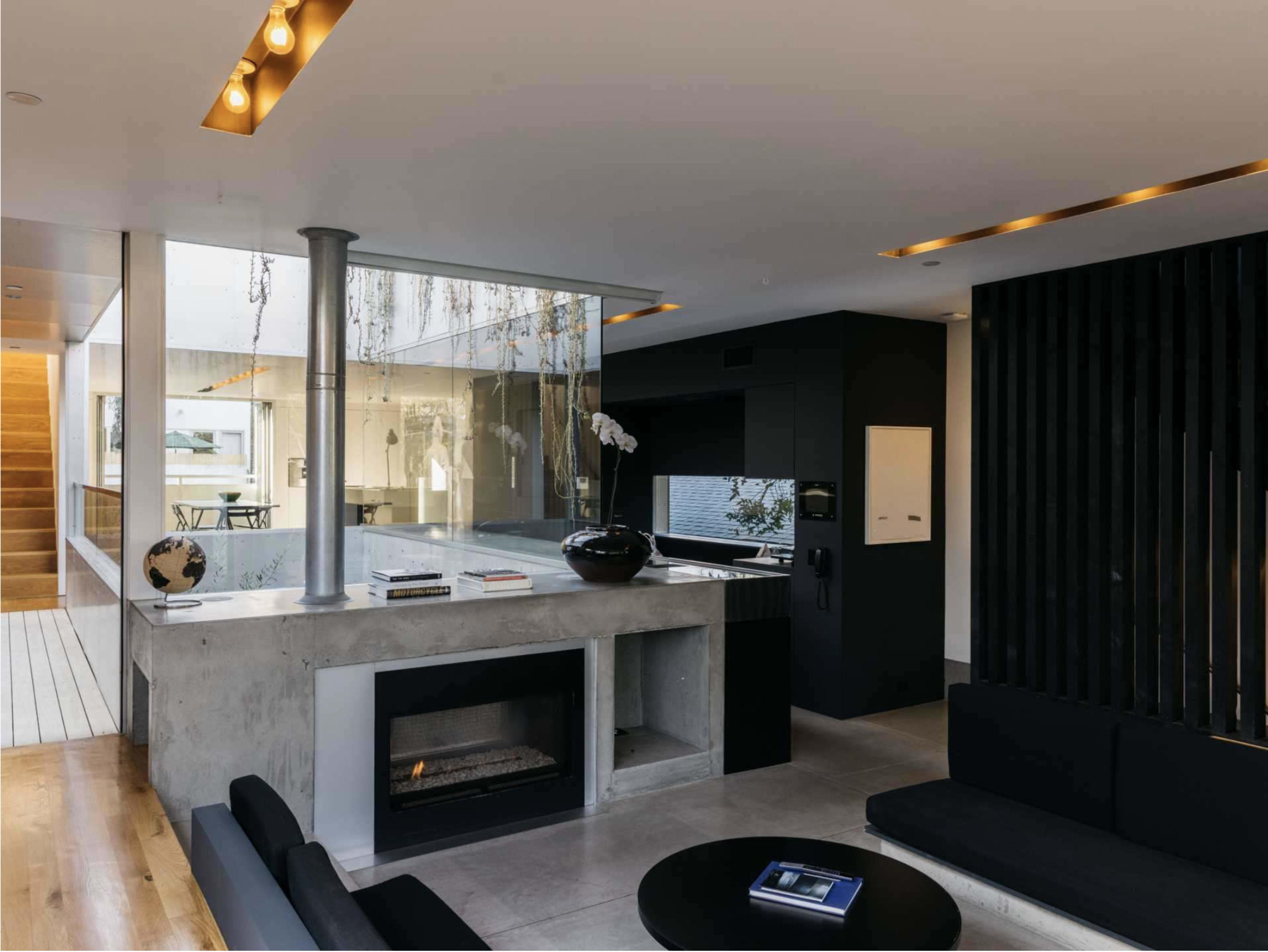 A modern living room with a concrete fireplace, glass walls, and minimalist furnishings.