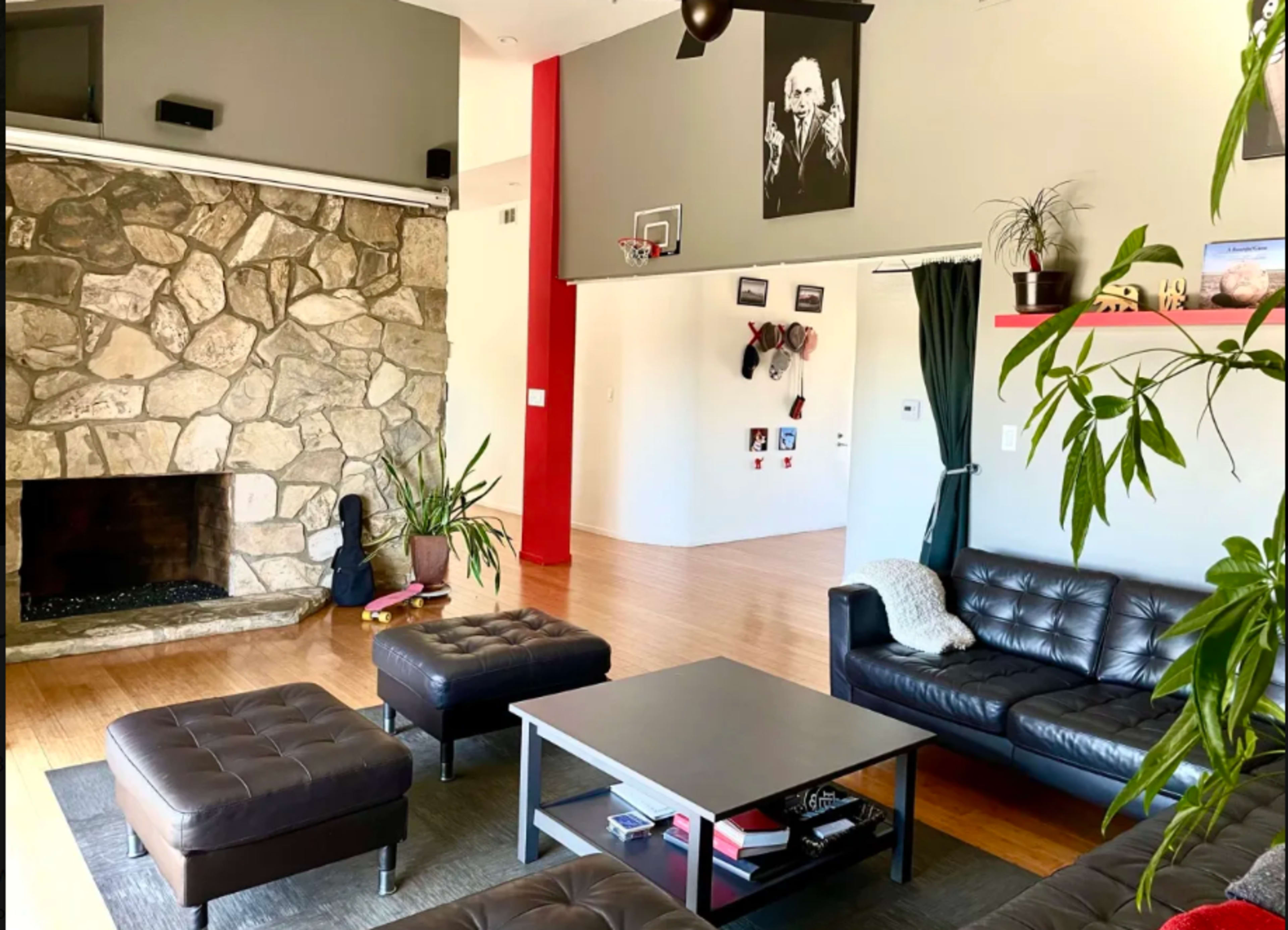 A modern living room featuring a stone fireplace, leather seating, a coffee table, and basketball hoop on the wall.