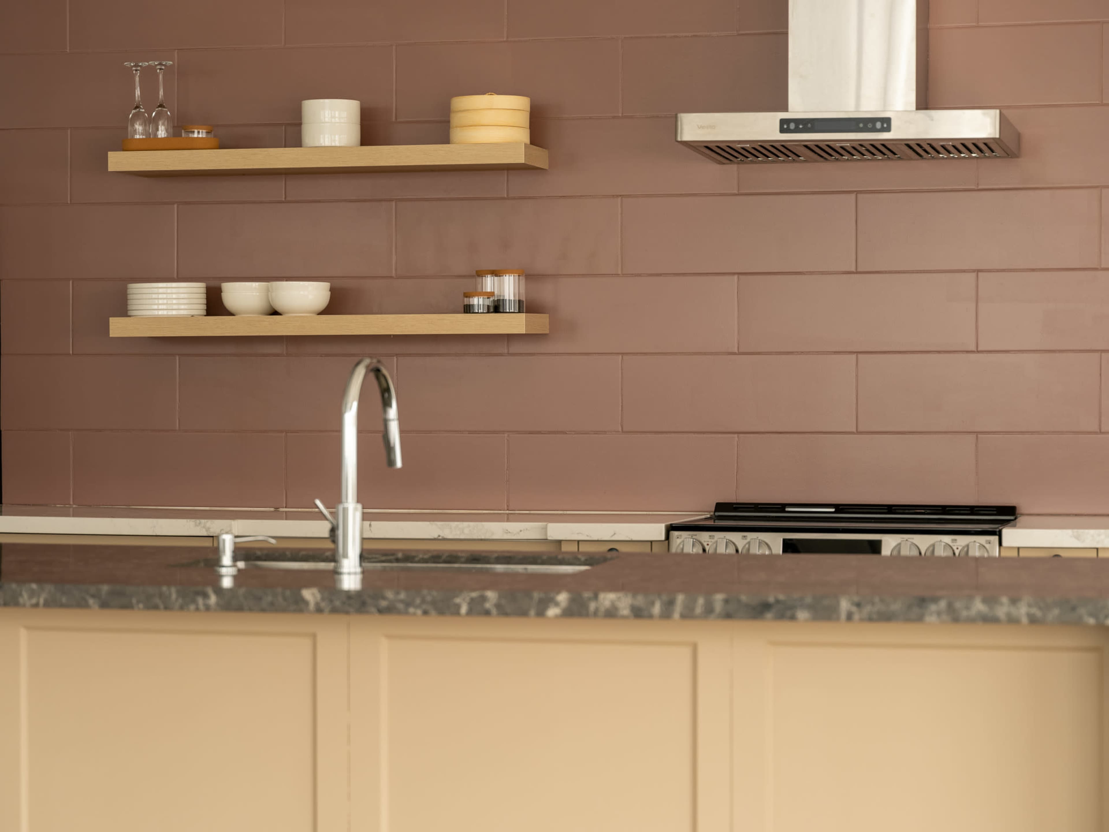 The image shows a modern kitchen with a countertop, wall-mounted shelves holding dishware, and a stove beneath a range hood.