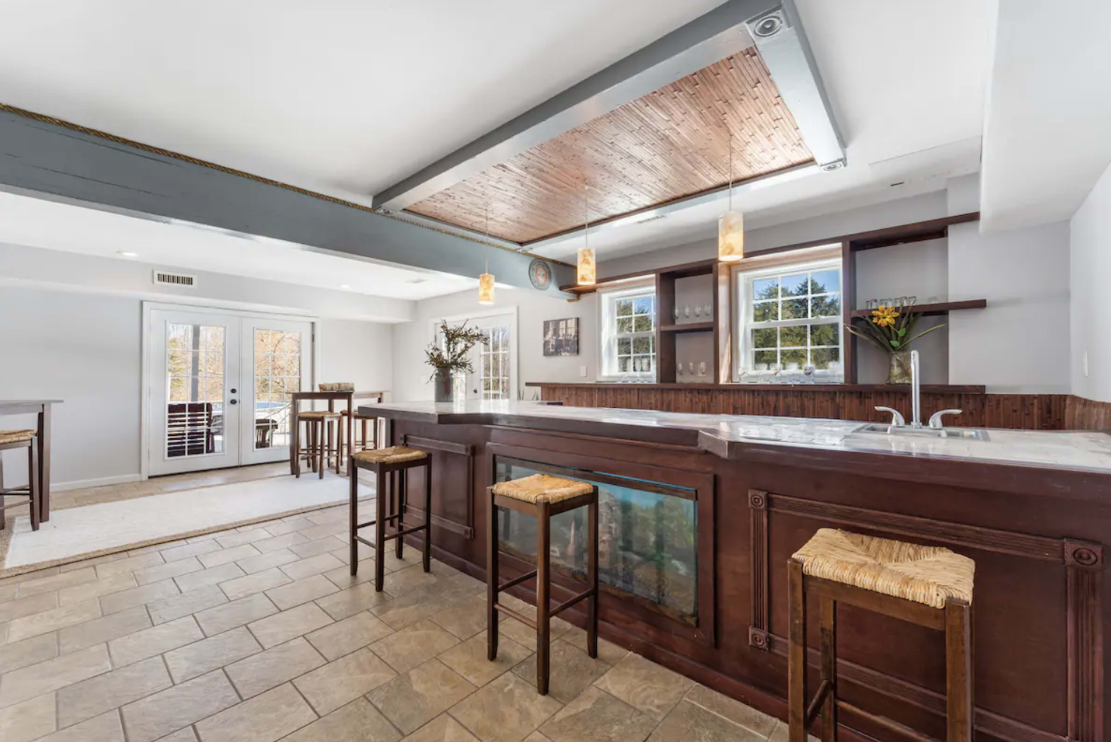 The image shows a spacious kitchen with a large island, wooden stools, and large windows overlooking a patio area.