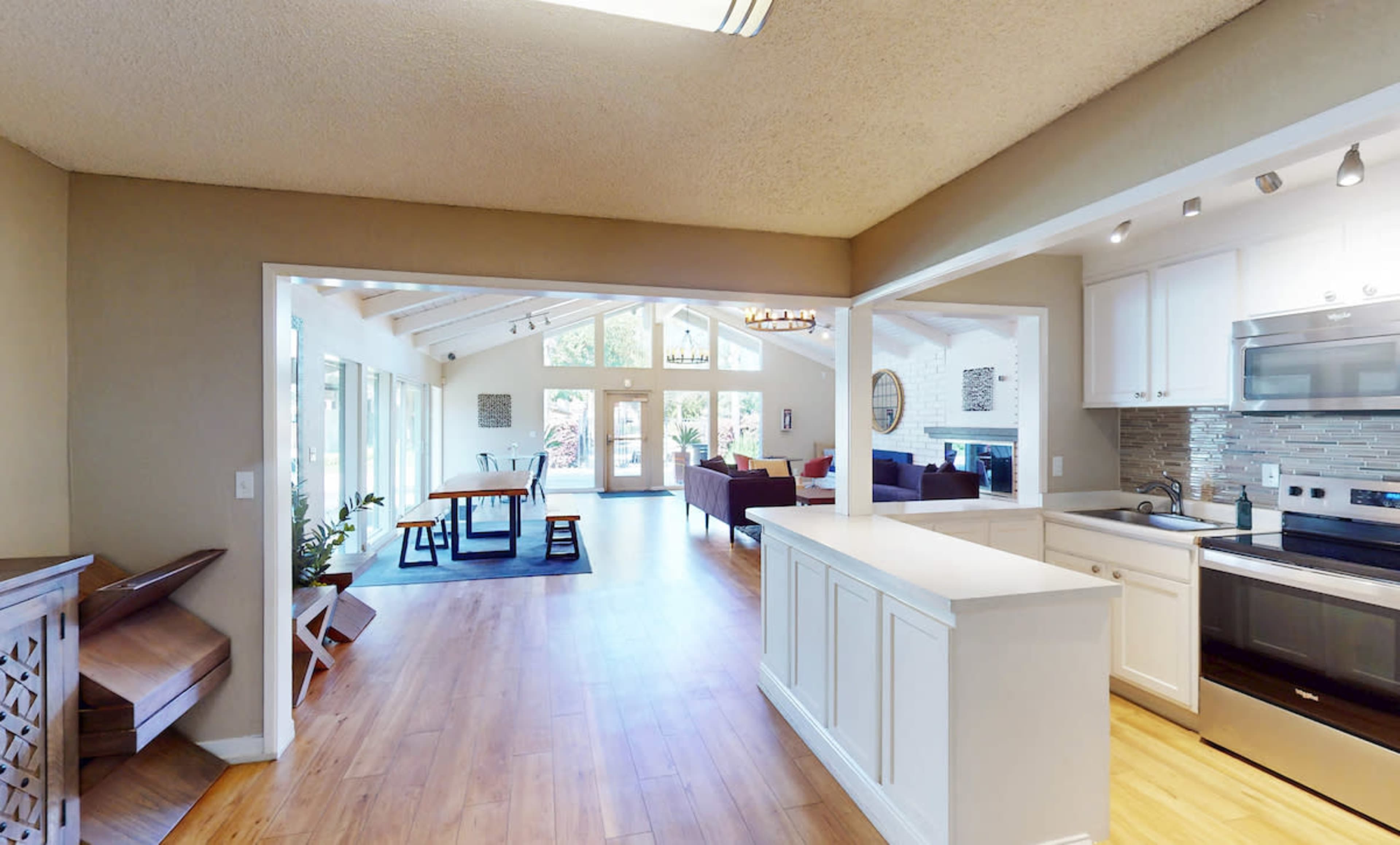 The image shows an open-concept living space with a kitchen, dining area, and seating area, featuring large windows that allow natural light to fill the room.