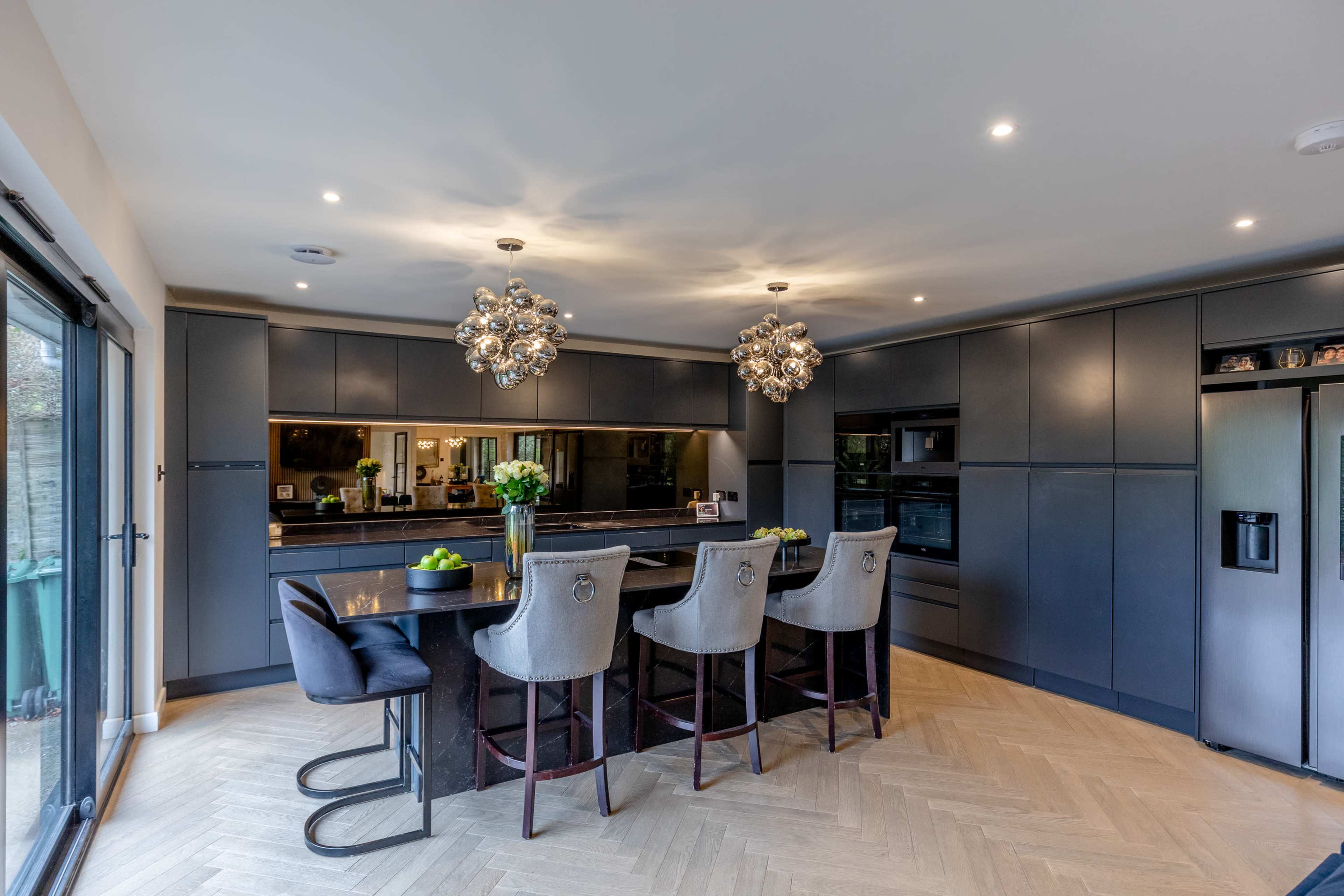 A modern kitchen features a large island with seating, dark cabinetry, and decorative light fixtures.