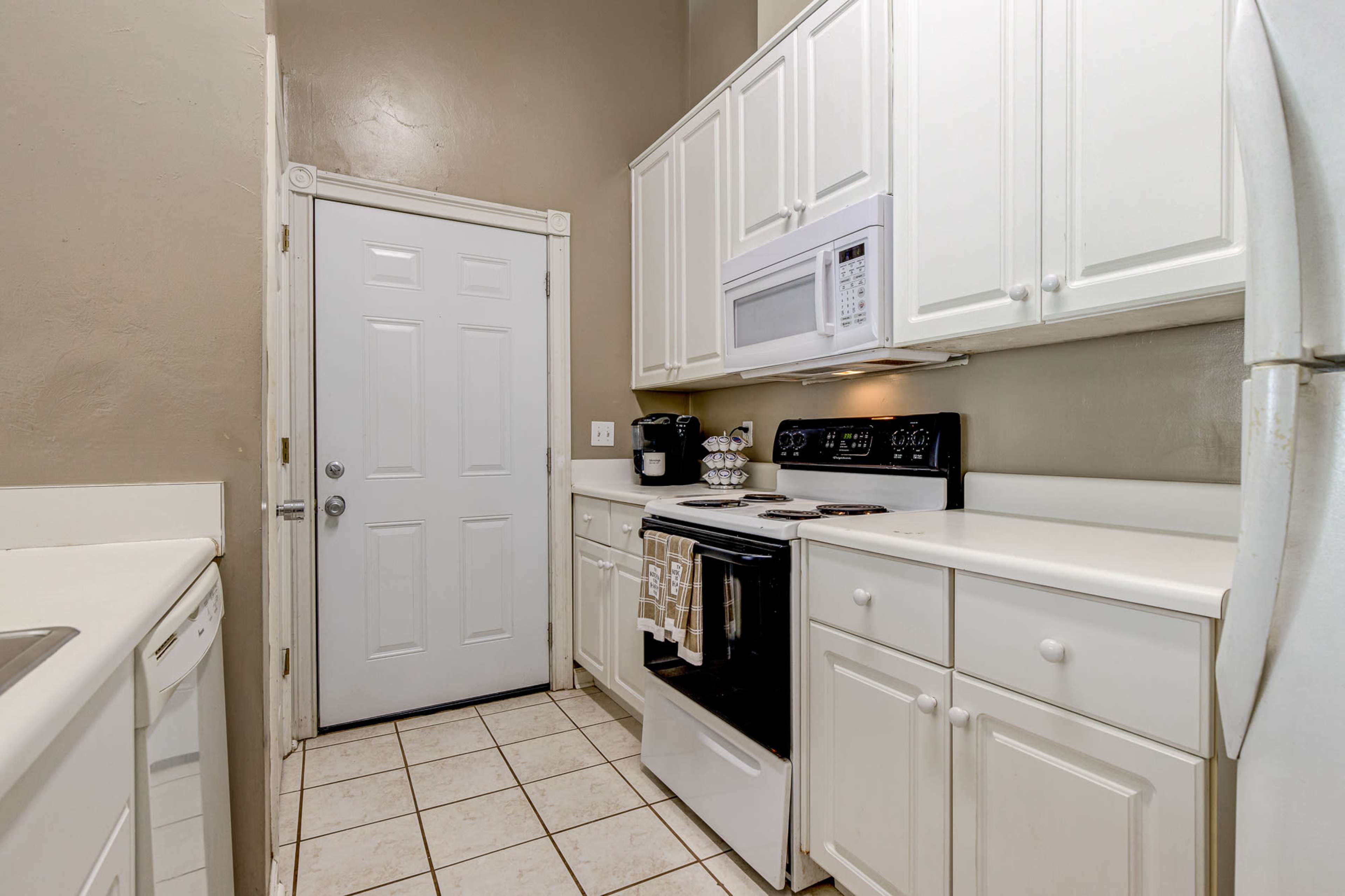 A compact kitchen featuring white cabinets, a black stove, a microwave, and a door leading outside.