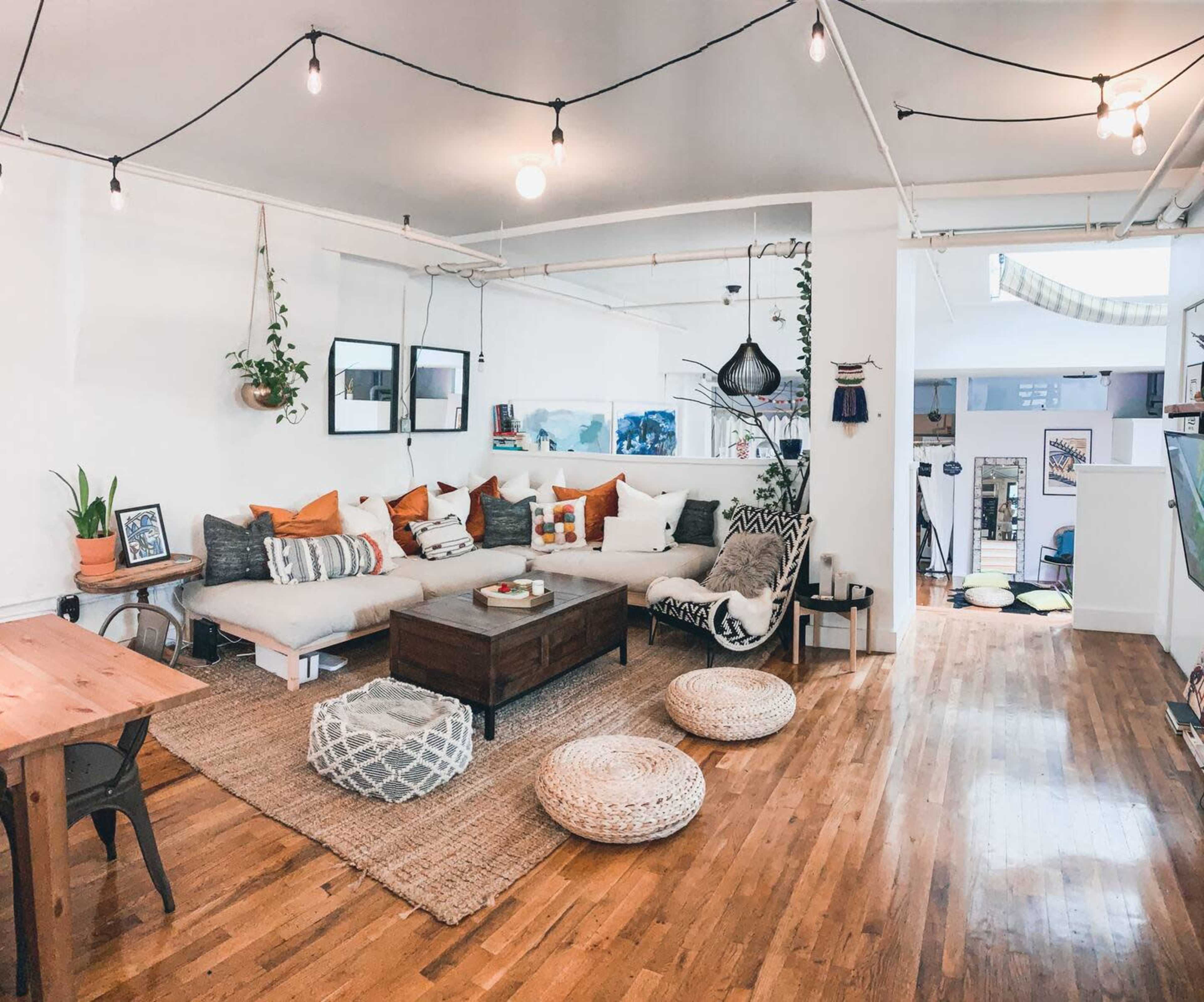 A cozy living room features a sectional sofa with colorful cushions, a wooden coffee table, and a woven rug, complemented by string lights and plants.
