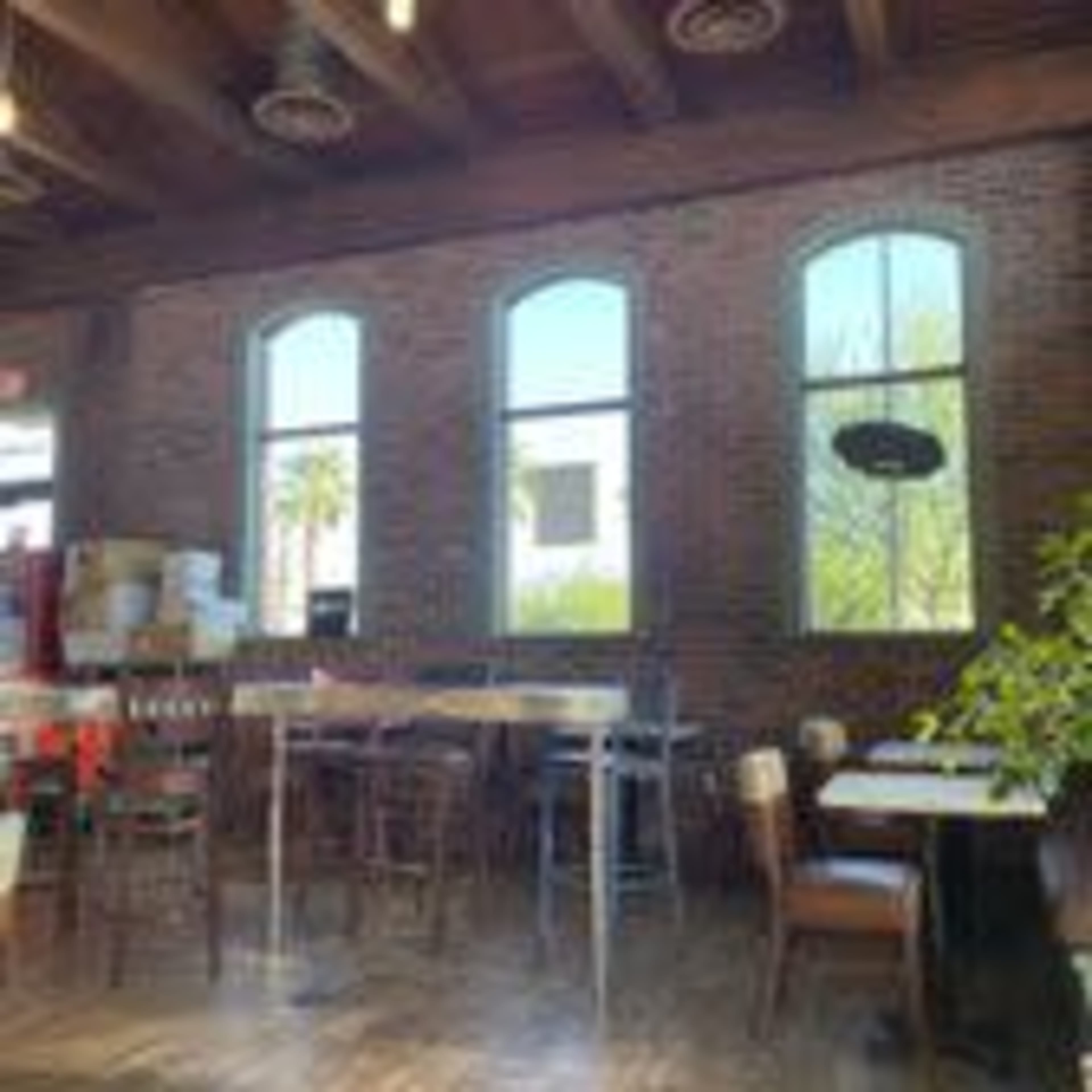 The interior of a restaurant featuring brick walls, tall windows, and wooden tables and chairs.
