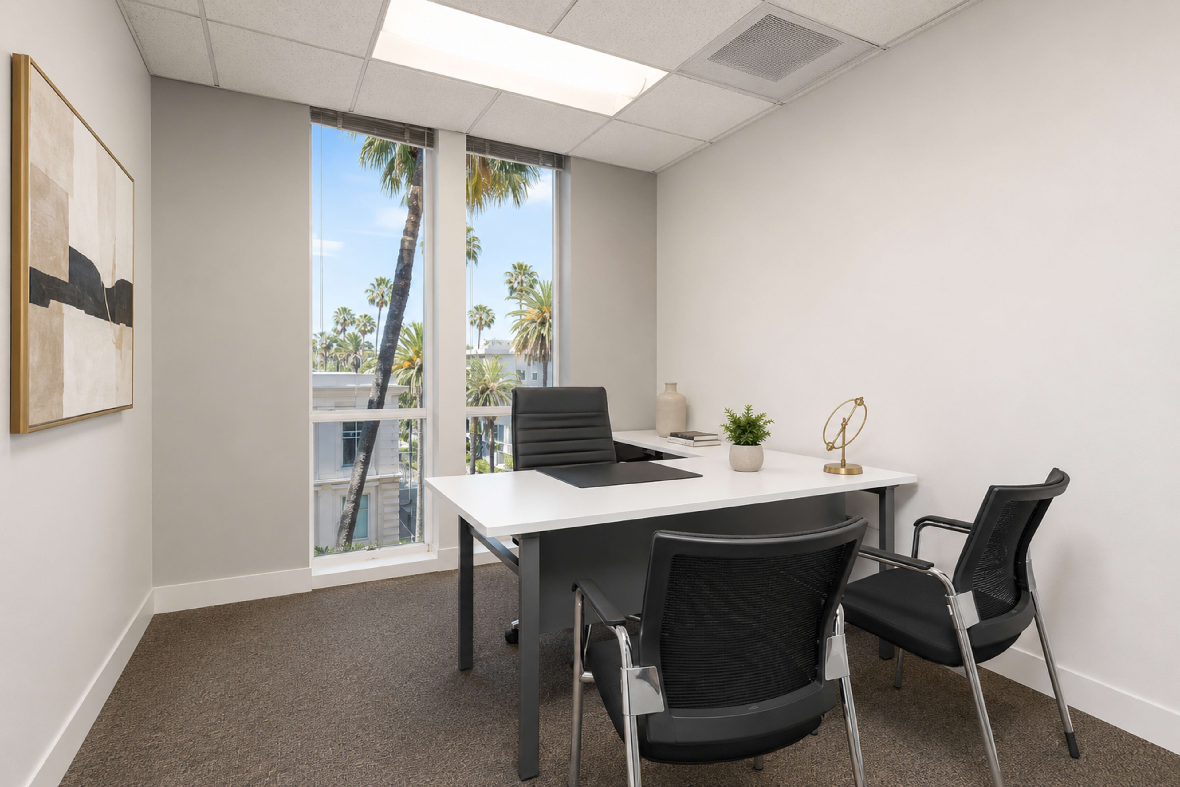 The image shows a well-lit office space featuring a white desk with a black chair, two black mesh chairs in front, and a large window with palm trees visible outside.