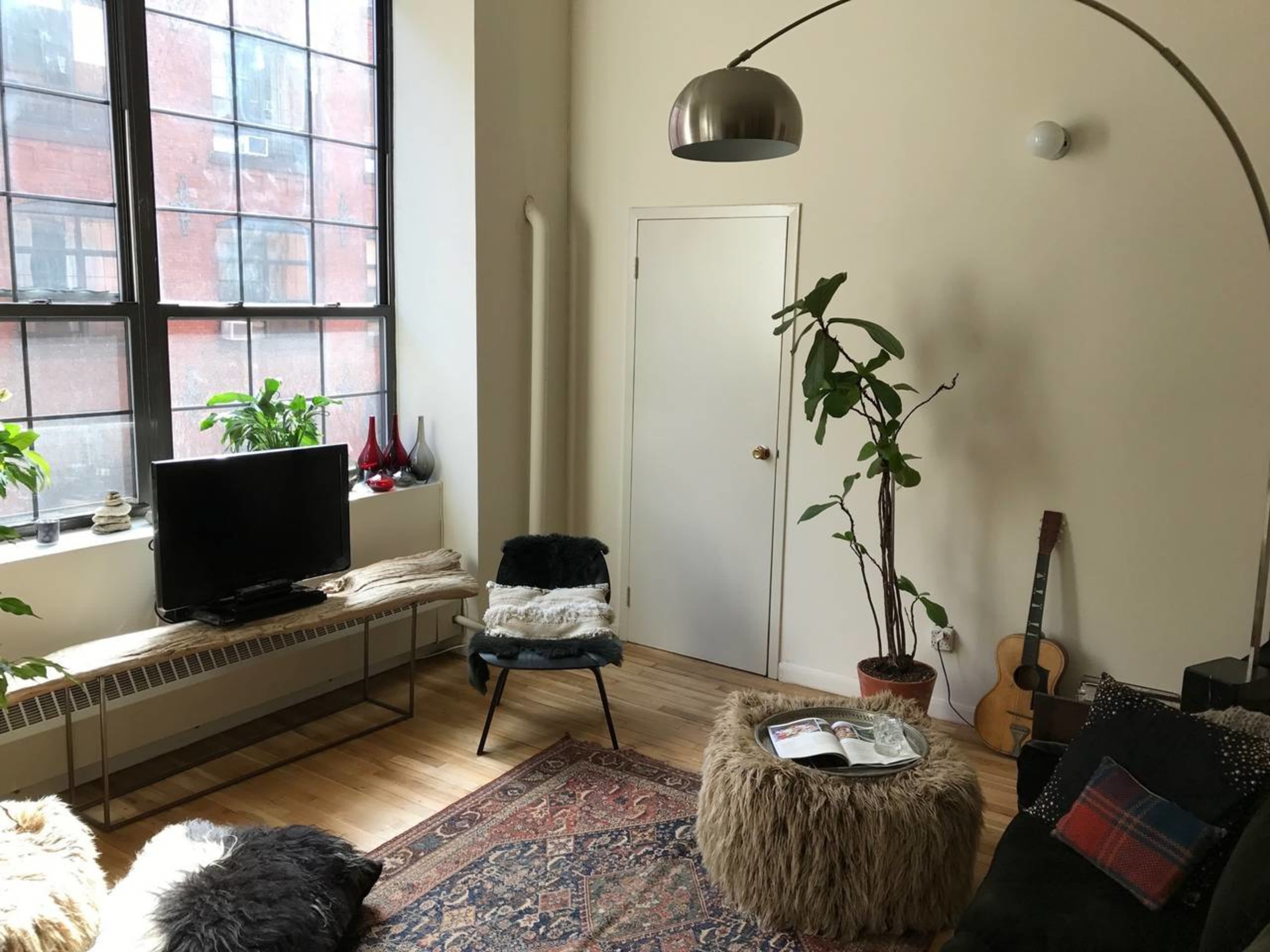 The image shows a cozy living room with large windows, a TV, a guitar, and furniture featuring a mix of textures.