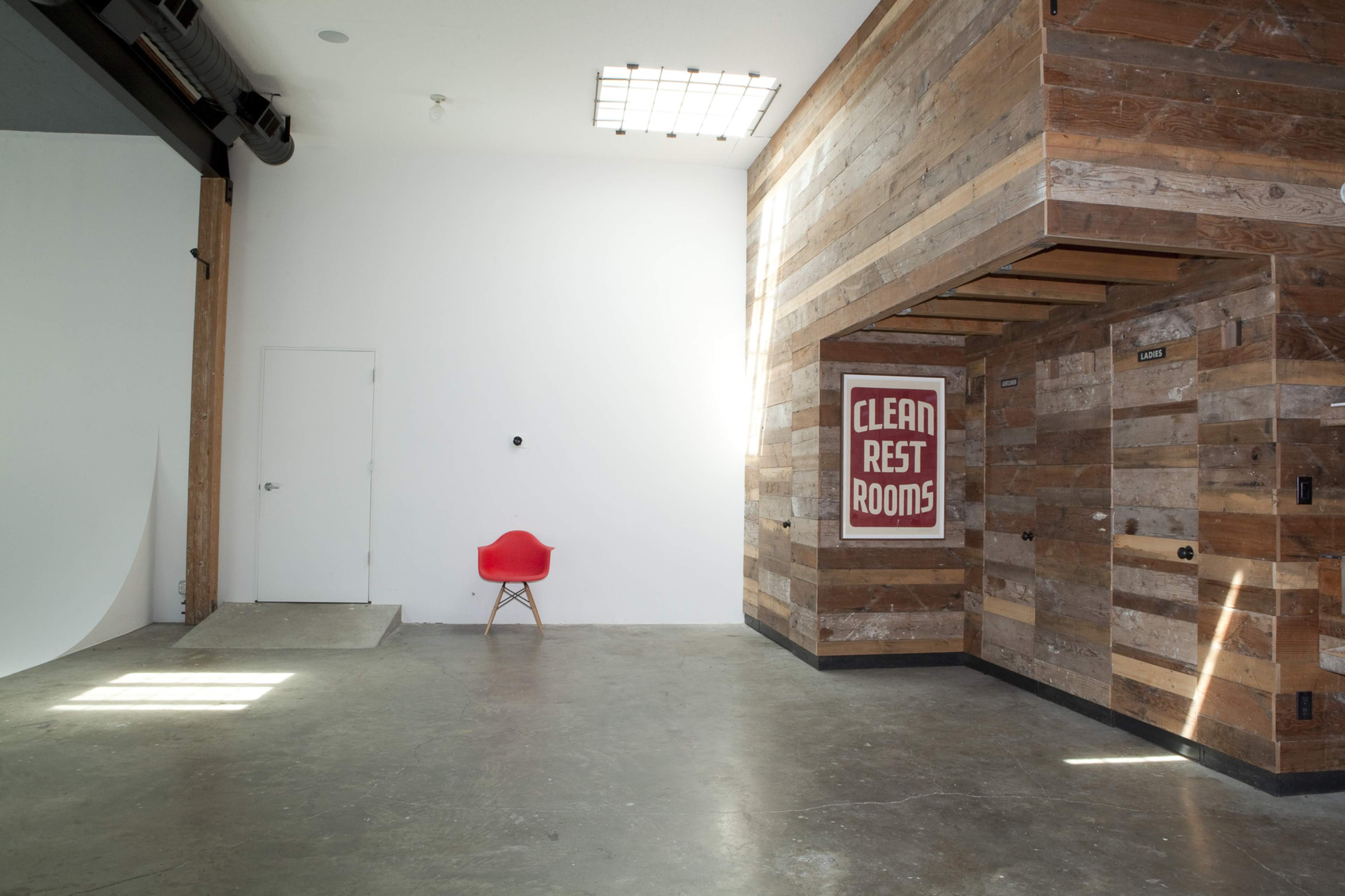 A spacious interior with a polished concrete floor, a wooden wall, a red chair, and a sign that reads "CLEAN REST ROOMS."