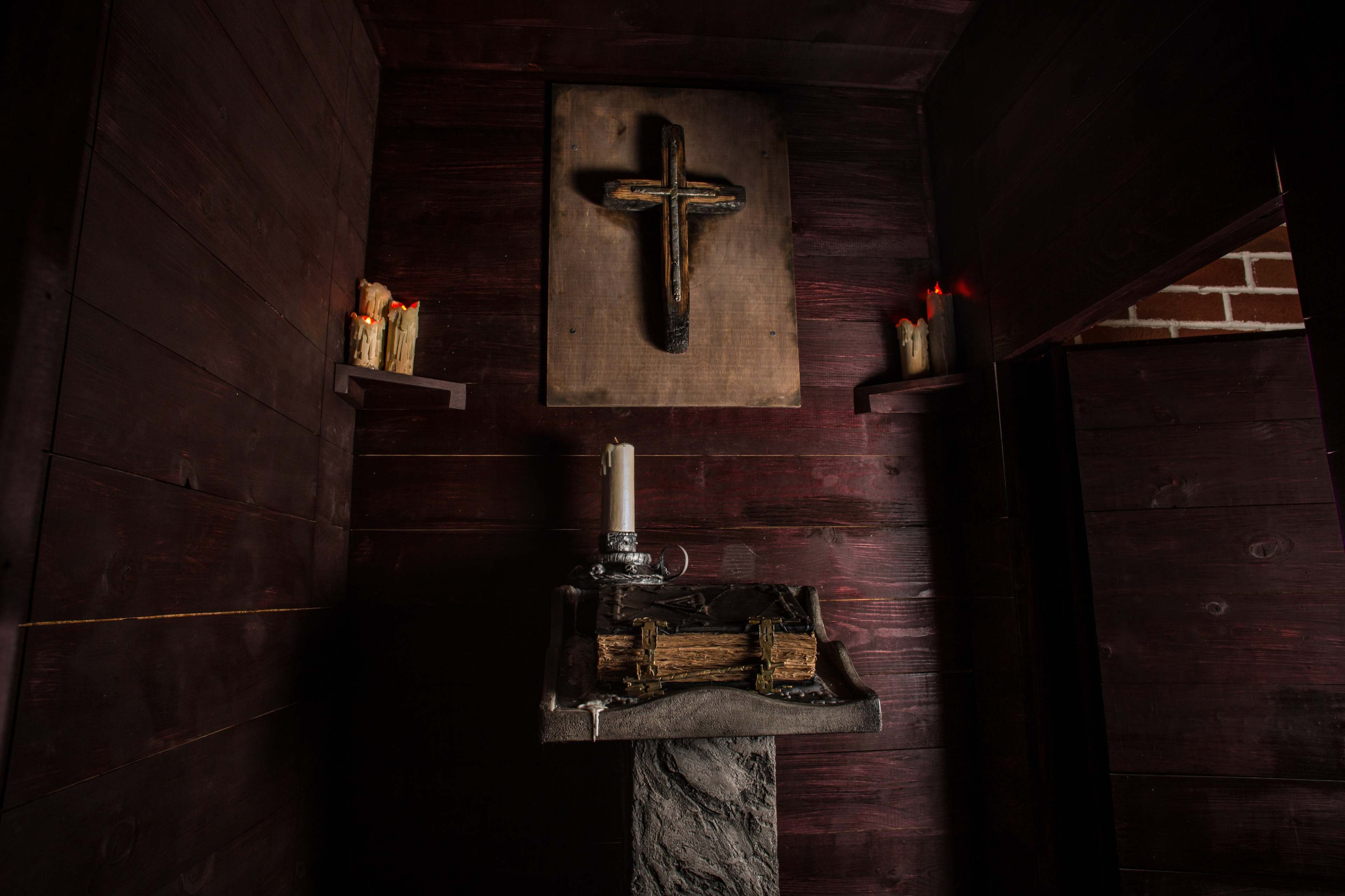 A dimly lit wooden alcove featuring a cross on the wall and a candle-lit altar made of stone and wood.