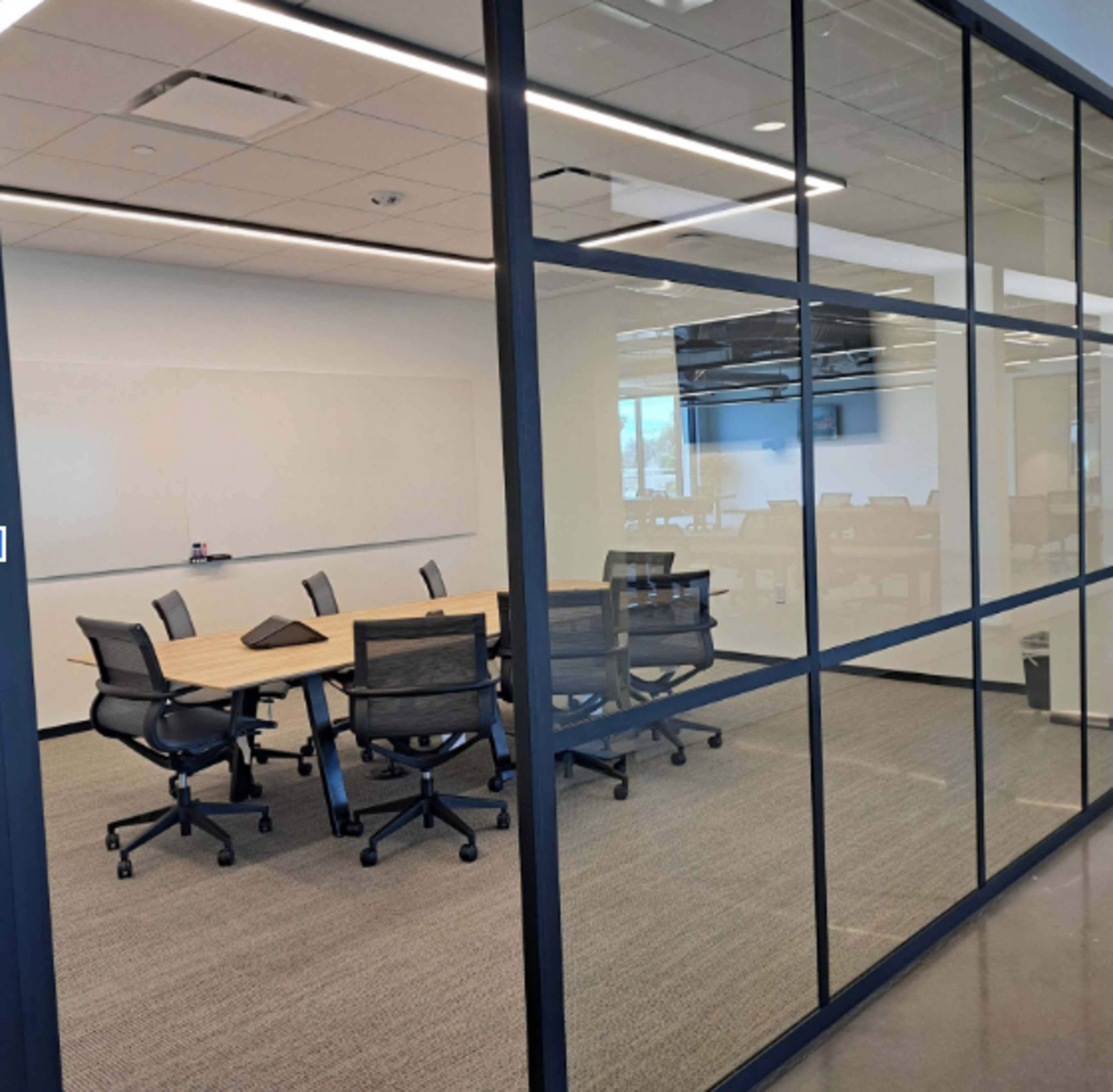 A conference room with a large table and several black chairs is visible through a glass wall.
