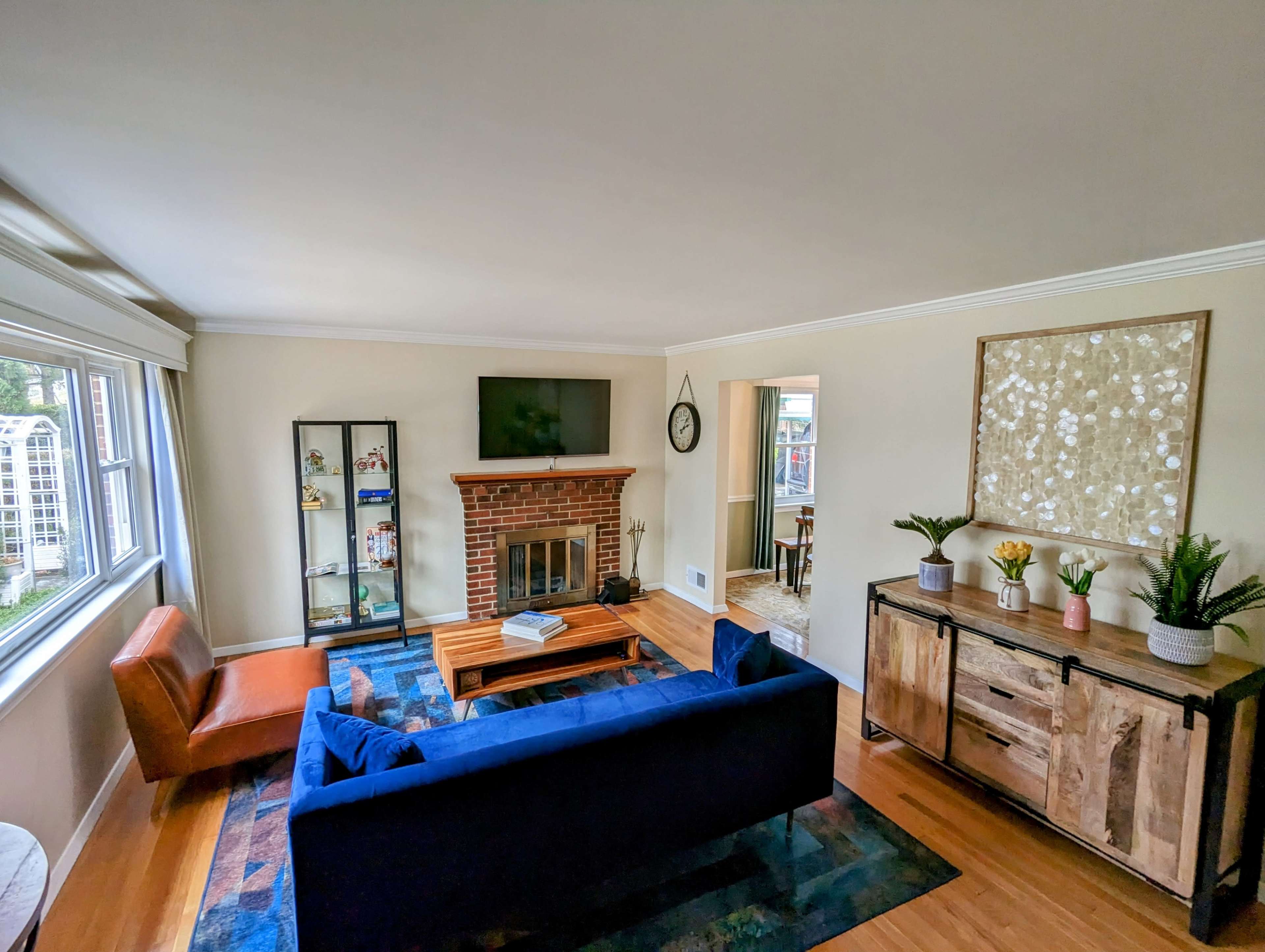 The living room features a blue sofa, a wooden coffee table, a brick fireplace, and a television mounted on the wall.