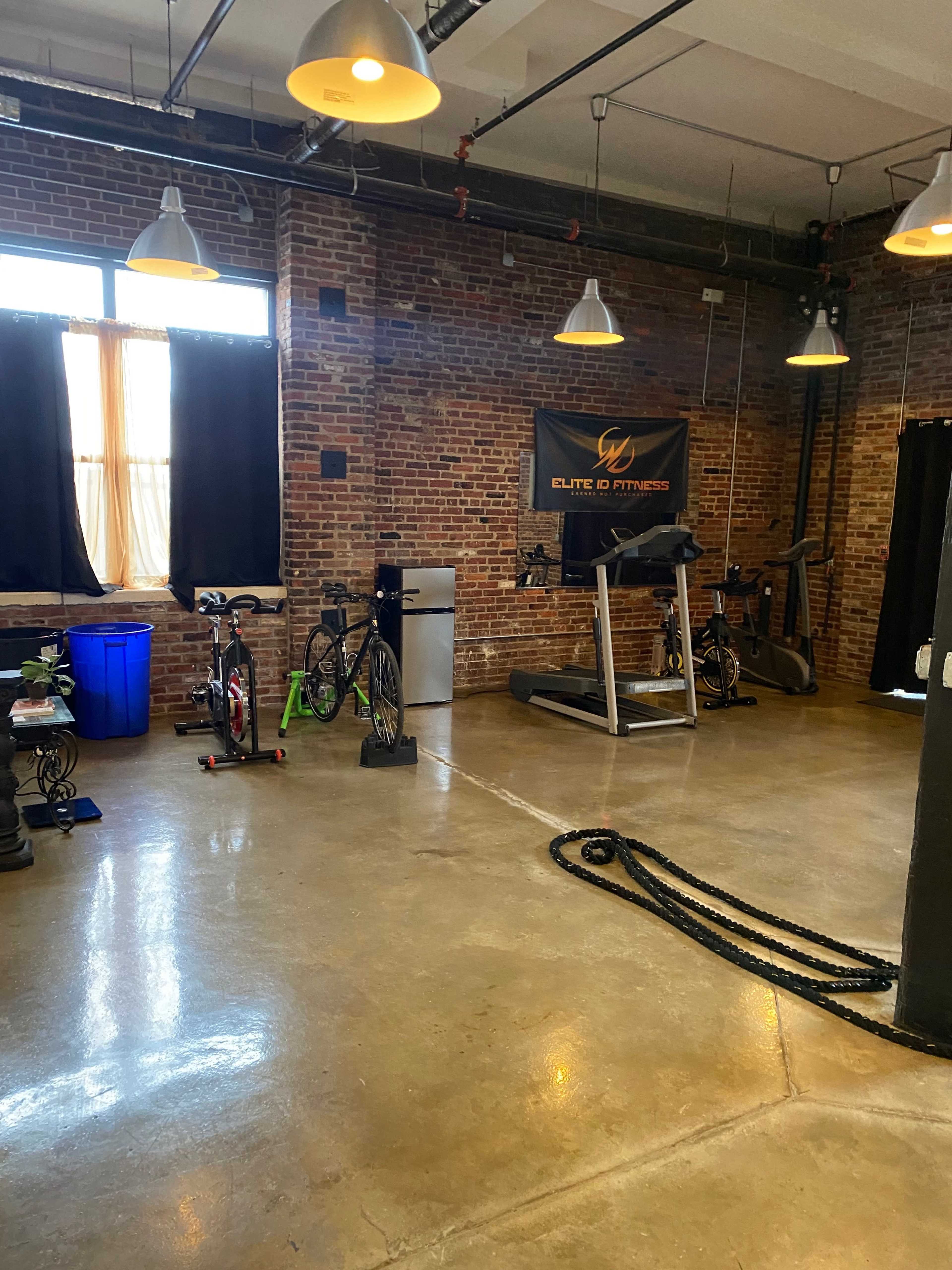 A fitness studio with exposed brick walls, workout equipment, and exercise bikes arranged around a clean, polished concrete floor.