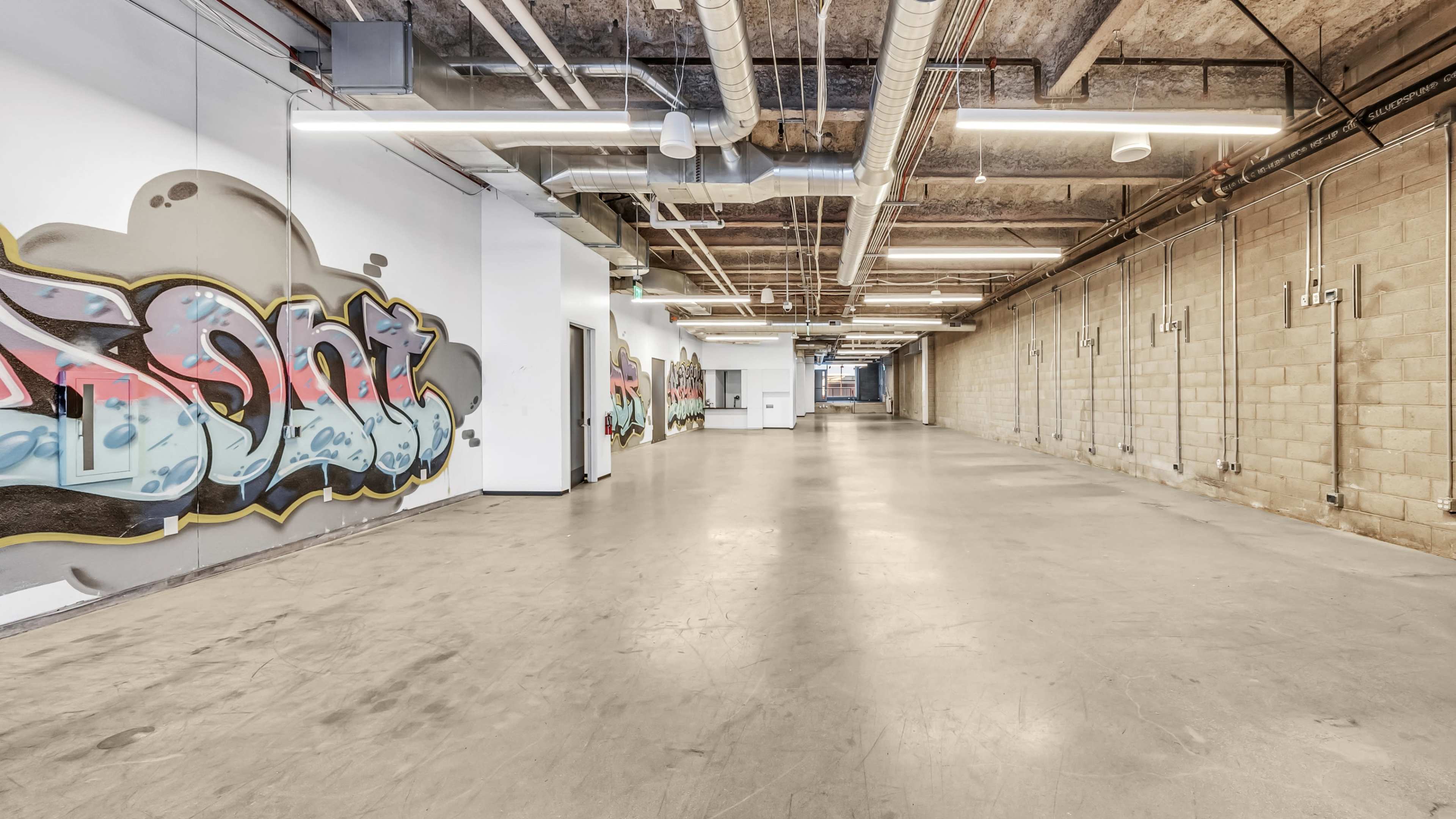 A spacious industrial corridor with graffiti-covered walls and exposed piping.