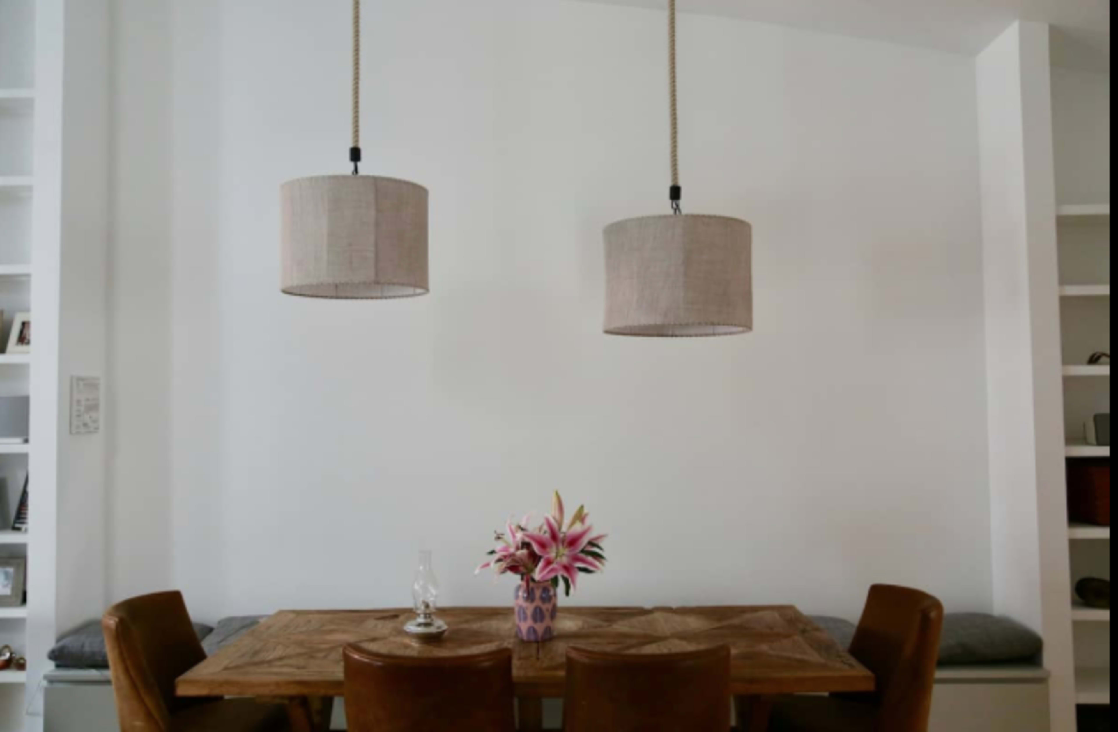 A dining area features a wooden table surrounded by leather chairs, with two pendant lamps hanging above and a vase of flowers on the table.