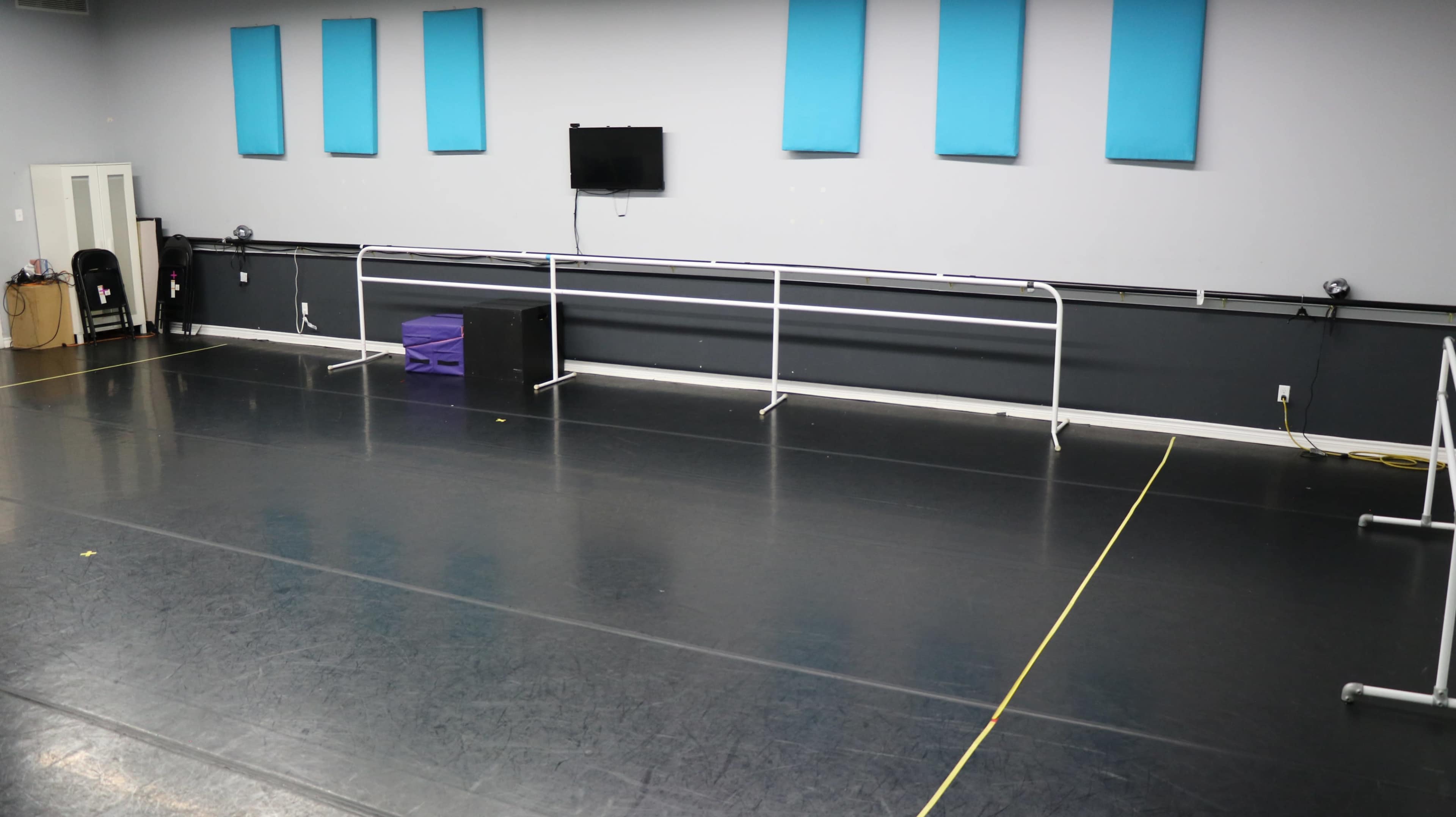 The image shows an empty dance studio with mirrored walls, a ballet barre along one side, and a television mounted on the wall.