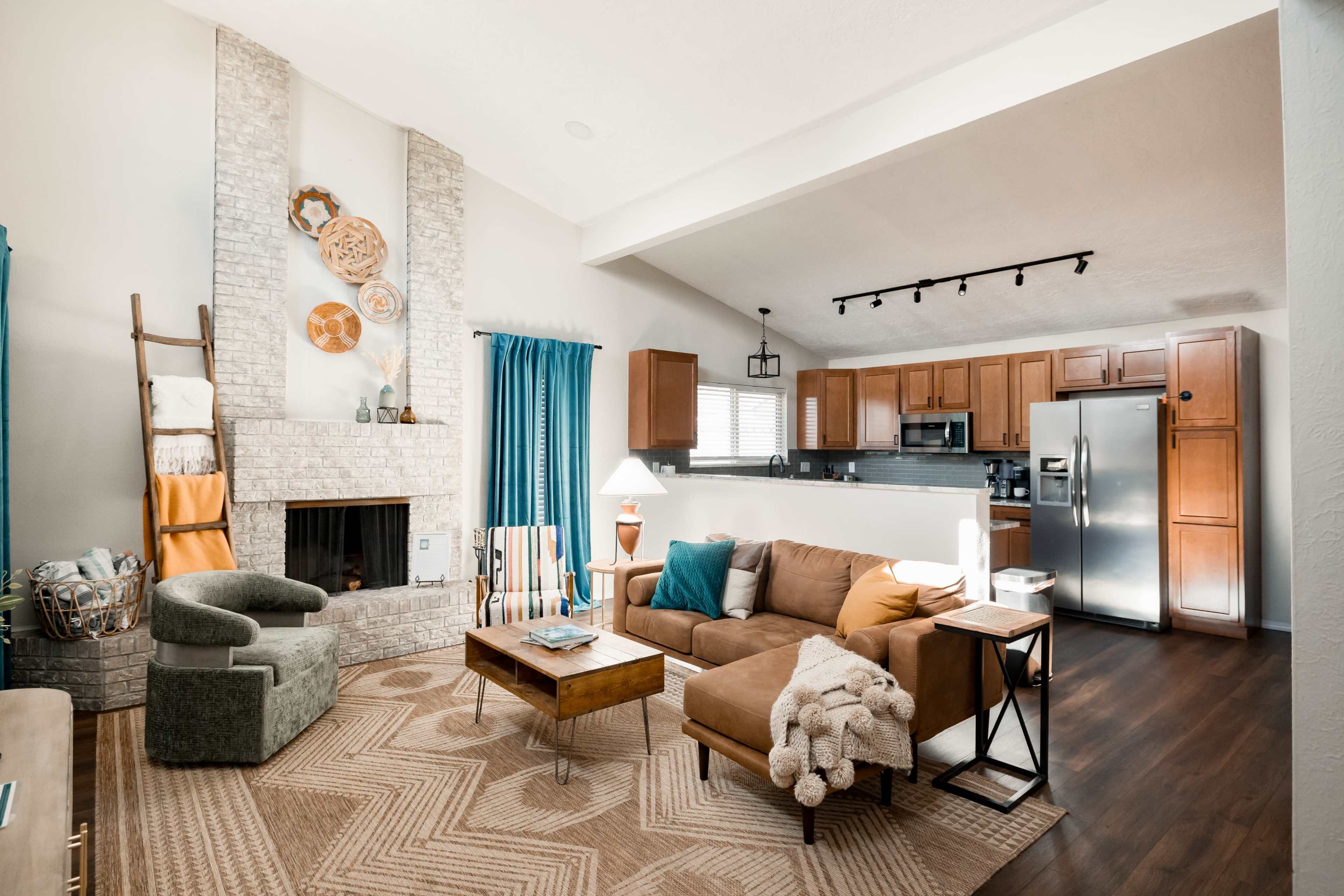 The living room features a cozy seating area with a brown sofa, a wooden coffee table, and a fireplace, adjacent to a kitchen with wooden cabinets and stainless steel appliances.