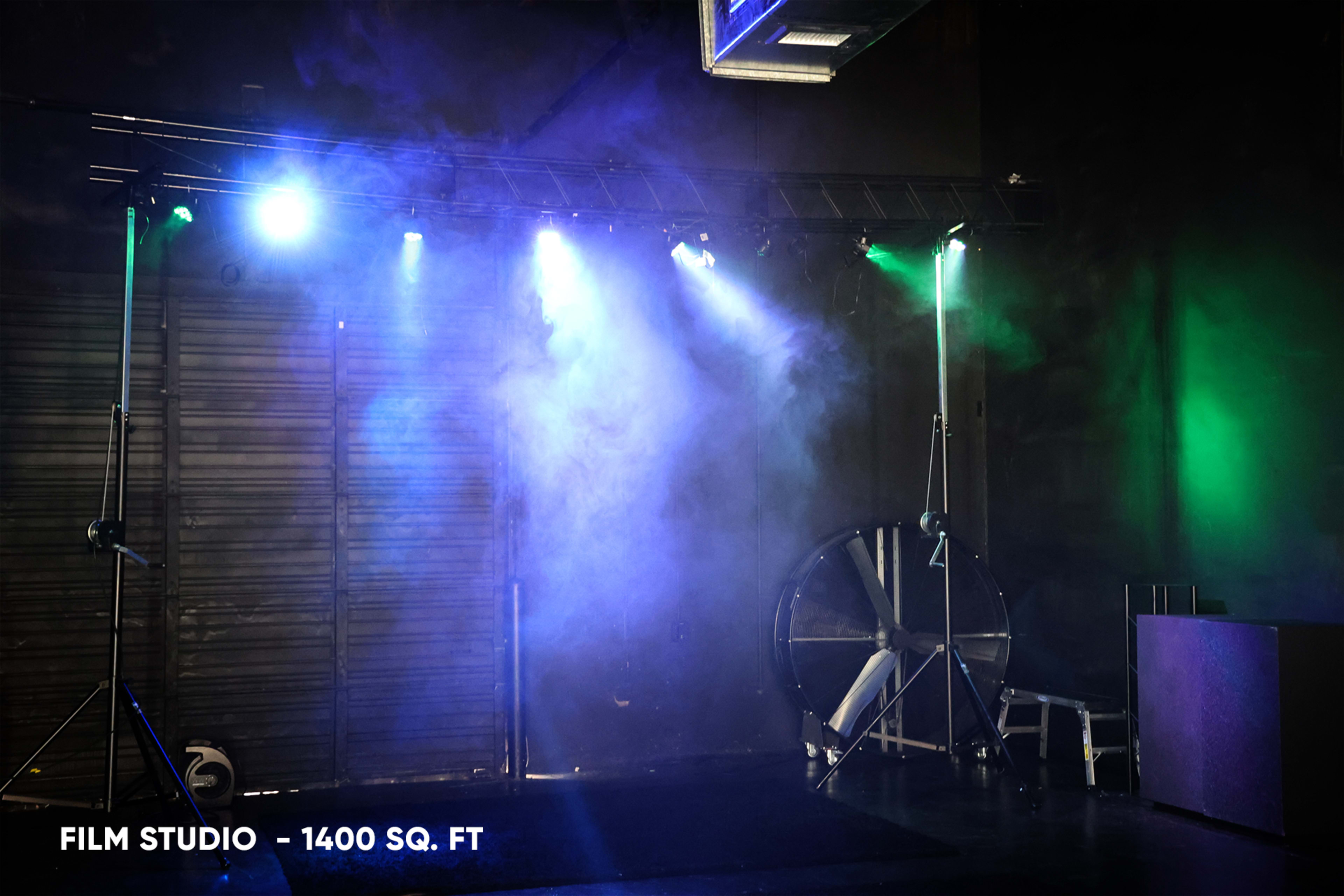 A film studio with smoke effects and colored lights illuminating a wide stage area.