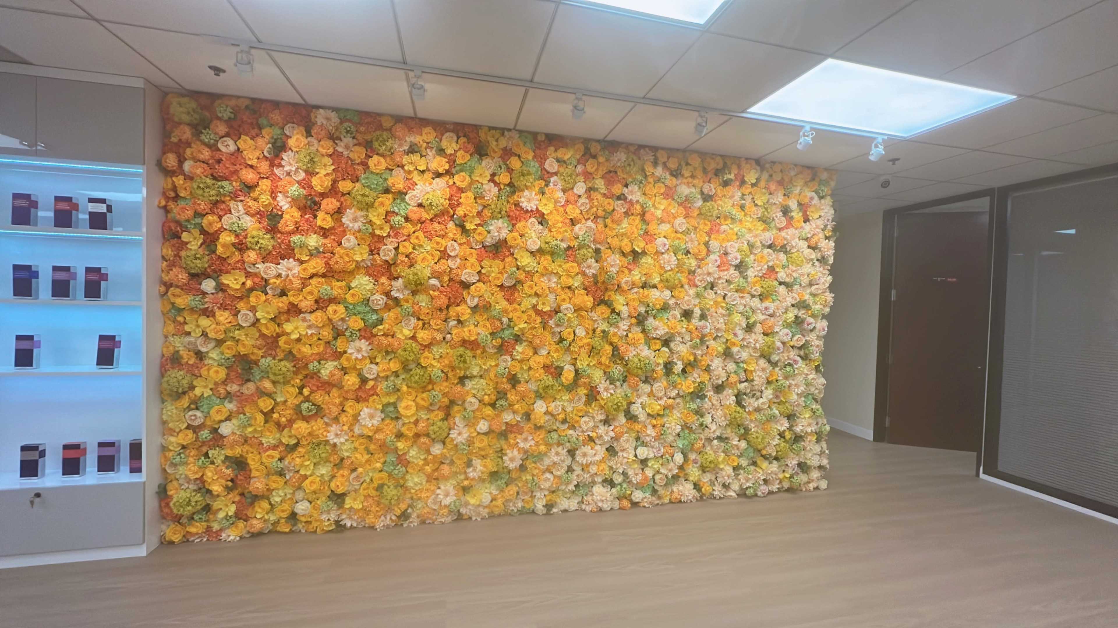 A wall covered in a vibrant arrangement of artificial flowers in various shades of orange, yellow, and cream.