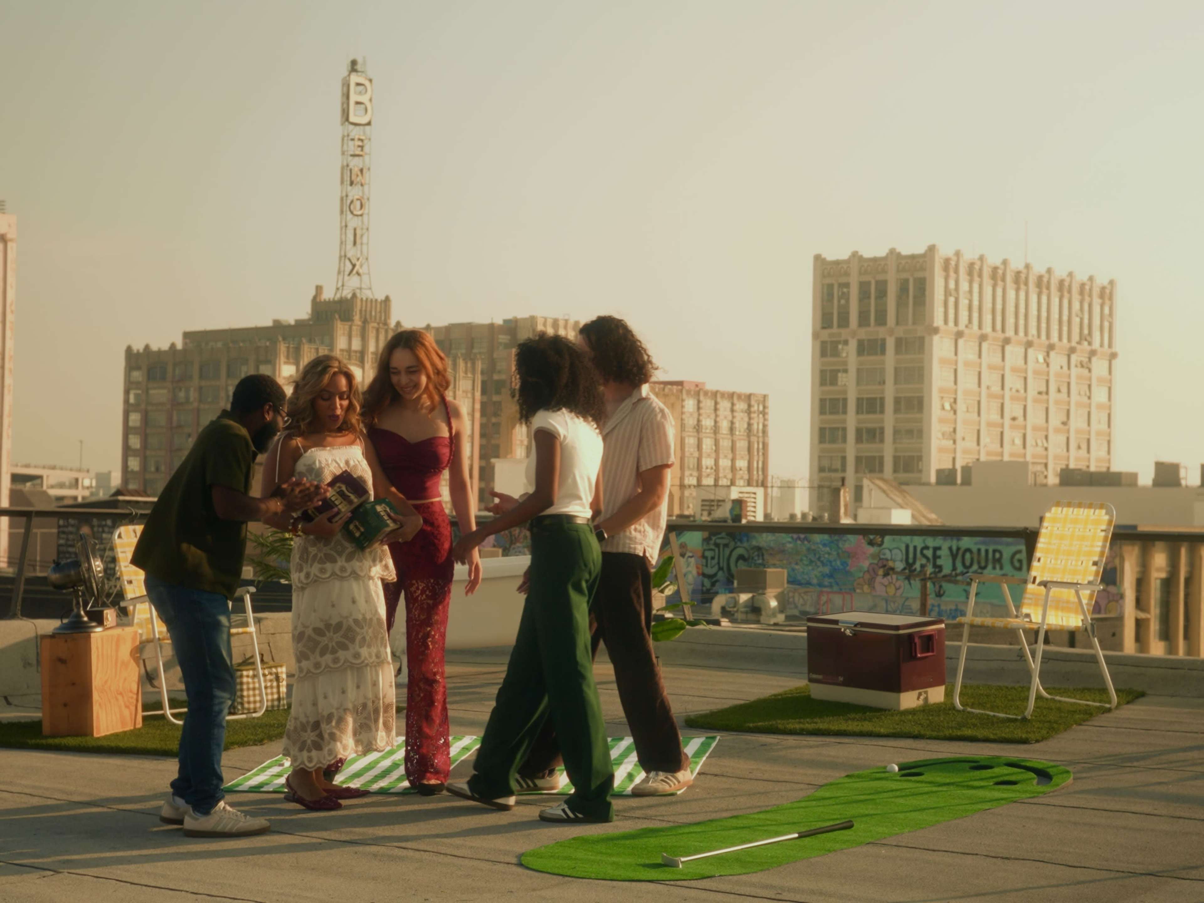 A group of five people interacts on a rooftop, with a city skyline and vintage buildings in the background.