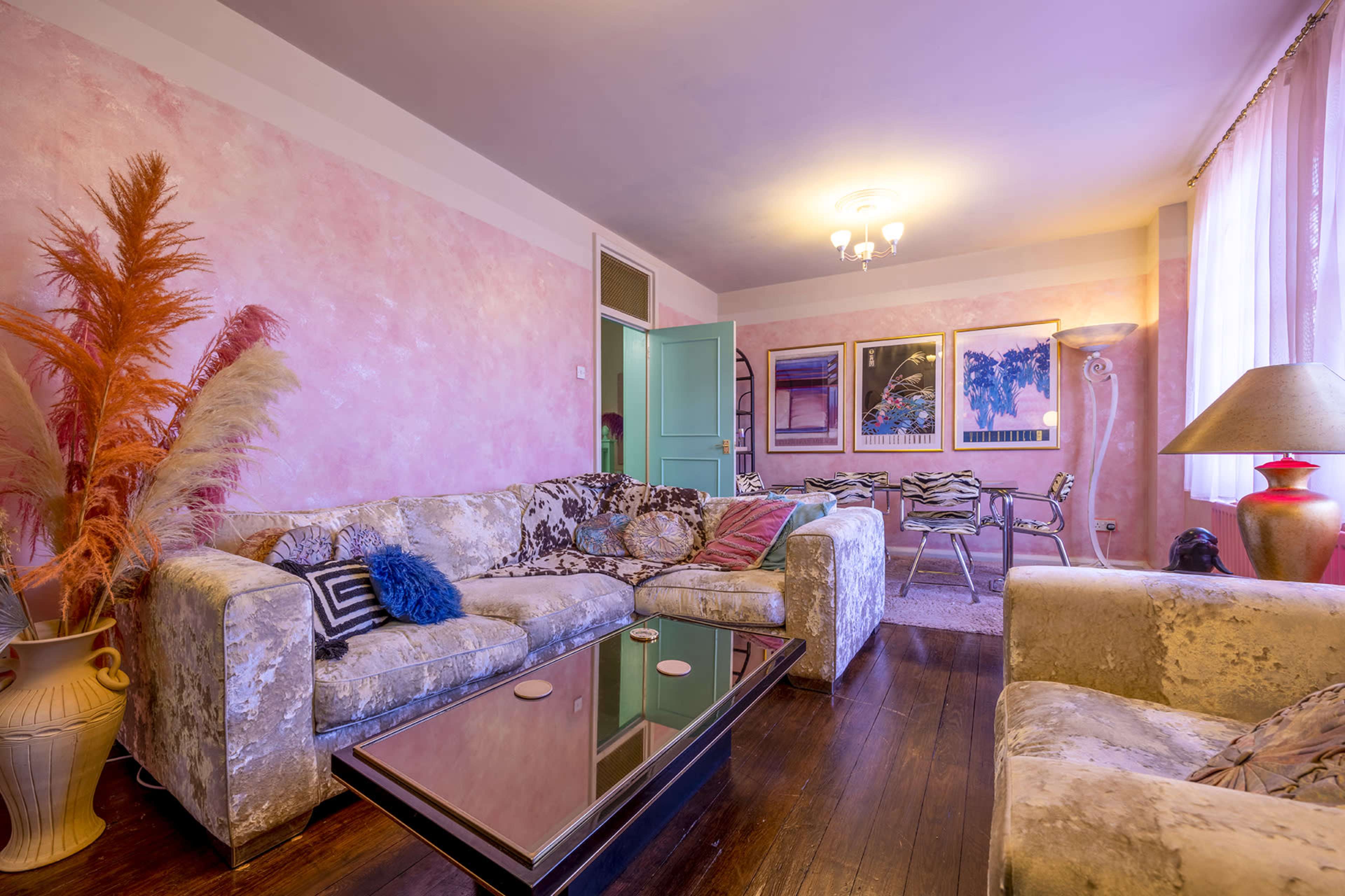 A living room features a patterned couch, a glass coffee table, and vibrant wall colors with artwork hanging nearby.