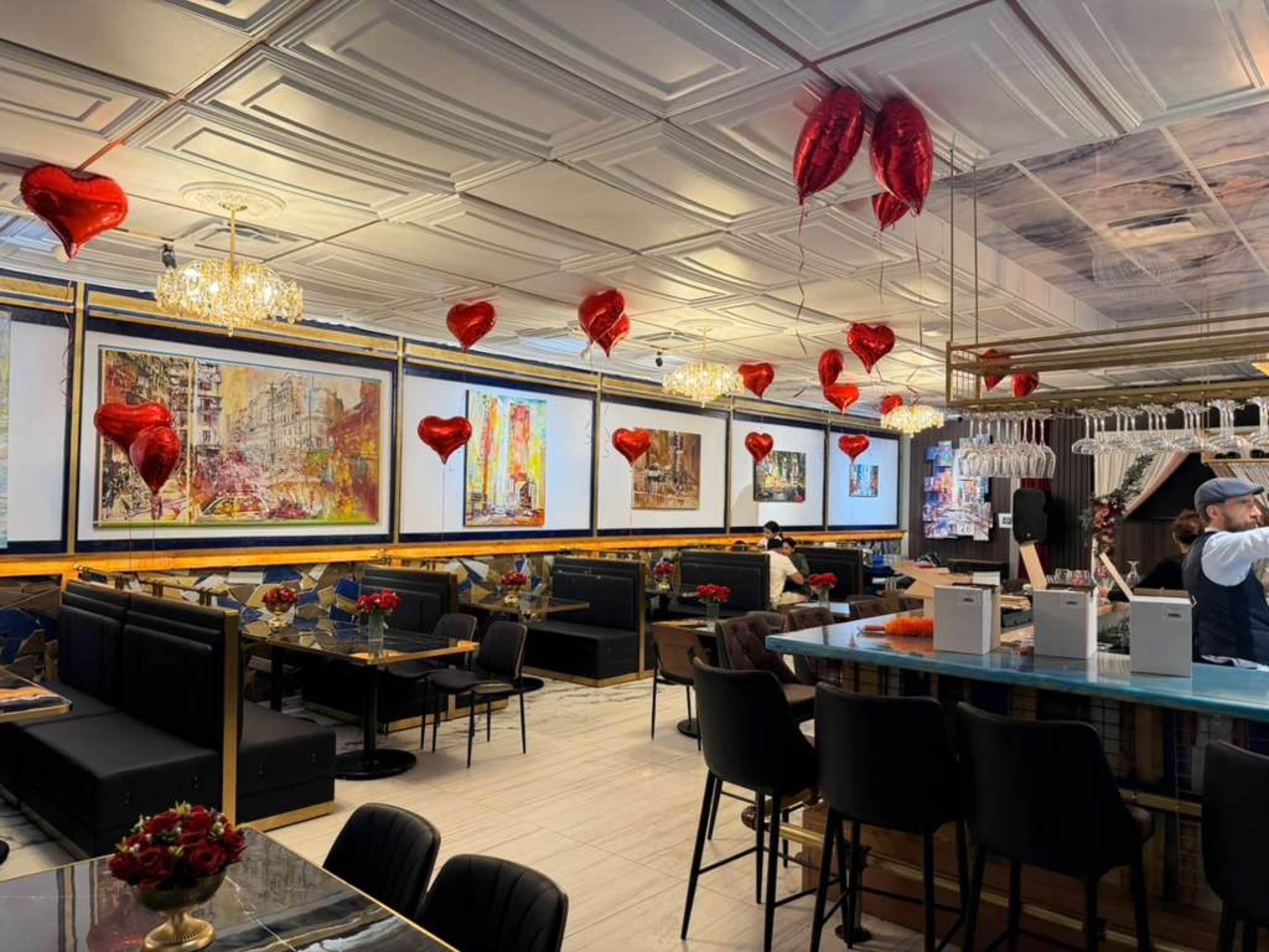 A restaurant interior features heart-shaped balloons, elegant lighting, and a mix of seating arrangements with artwork on the walls.