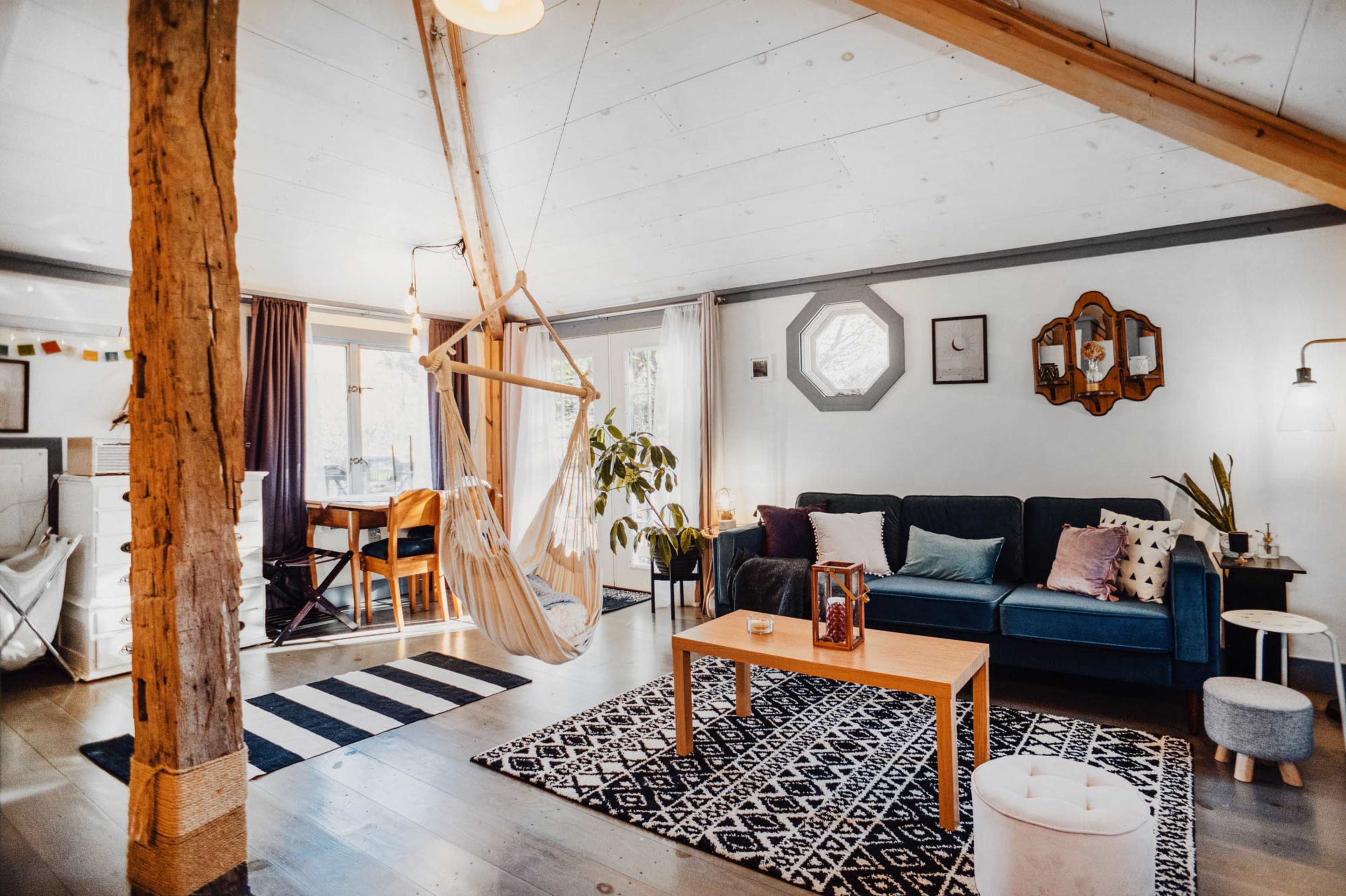 A modern living room with a hammock, a green sofa, a wooden coffee table, and a decorative rug on the floor.
