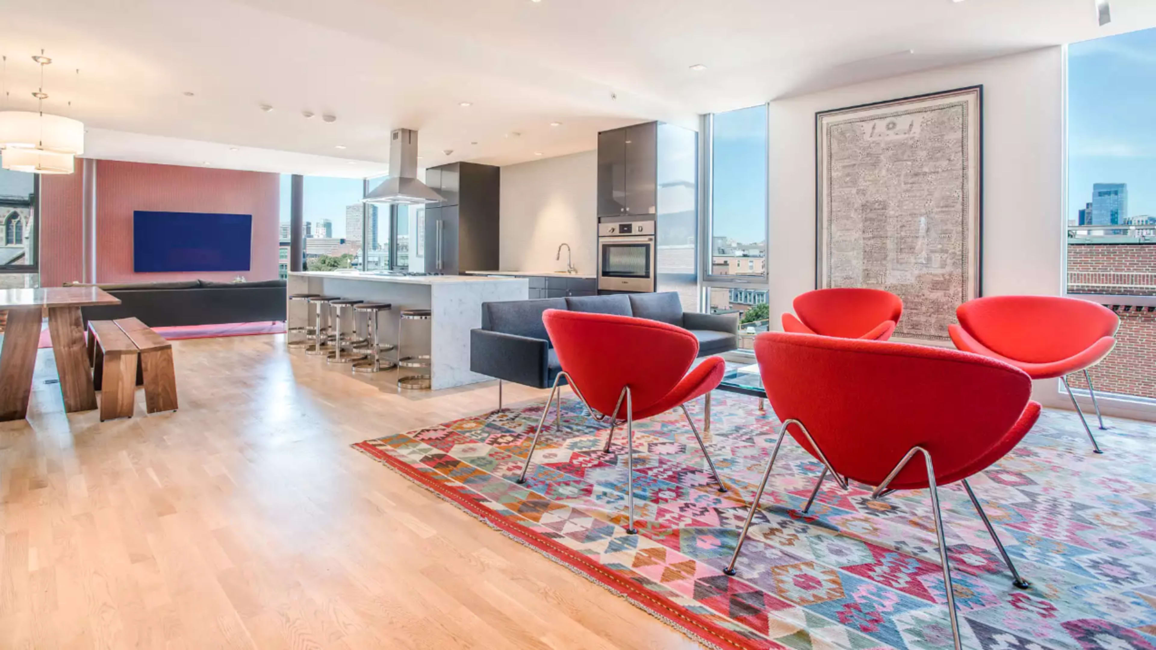 A modern open-concept living space featuring a kitchen, dining area, and seating area with bright red chairs on a patterned rug.