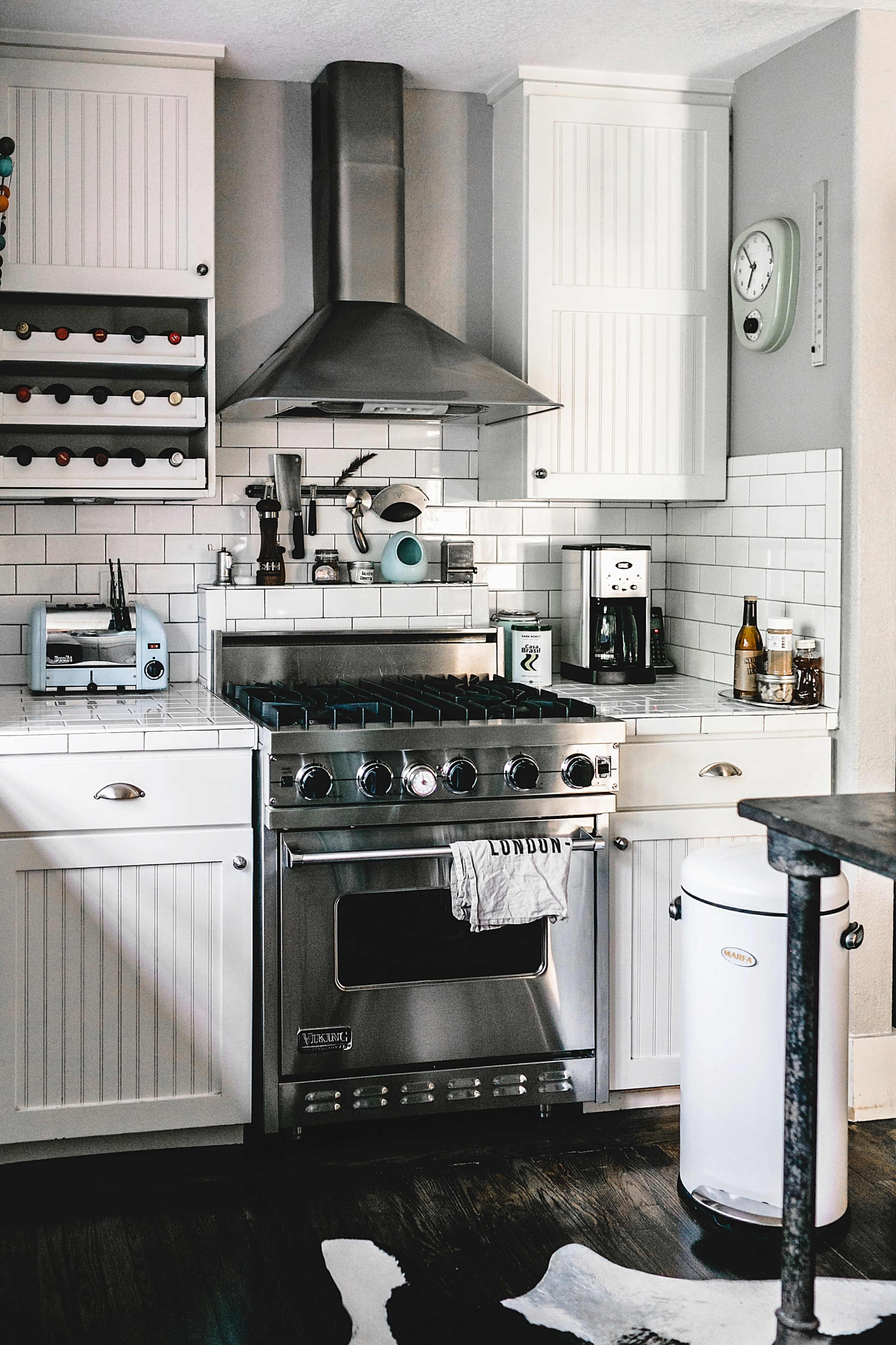 The image shows a modern kitchen featuring white cabinets, a stainless steel gas stove with an overhead hood, a coffee maker, and a wine rack.