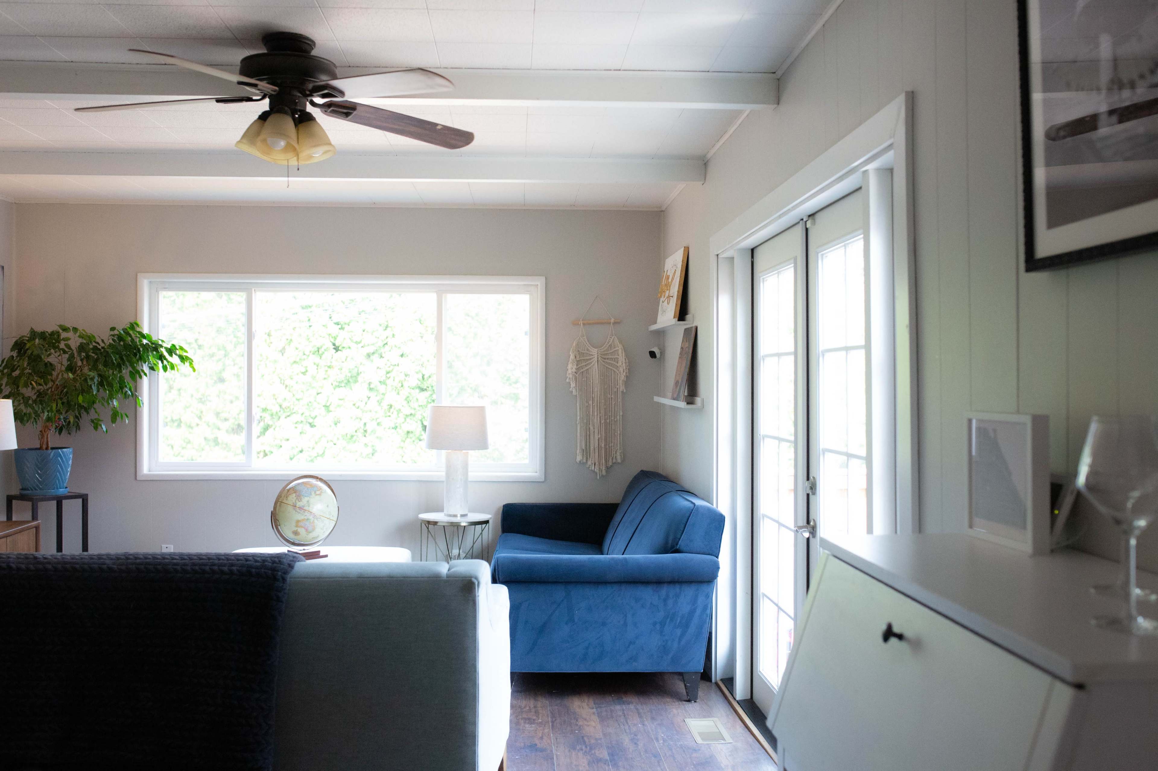 A living room features a blue couch, a globe on a side table, a ceiling fan, and large windows with natural light.
