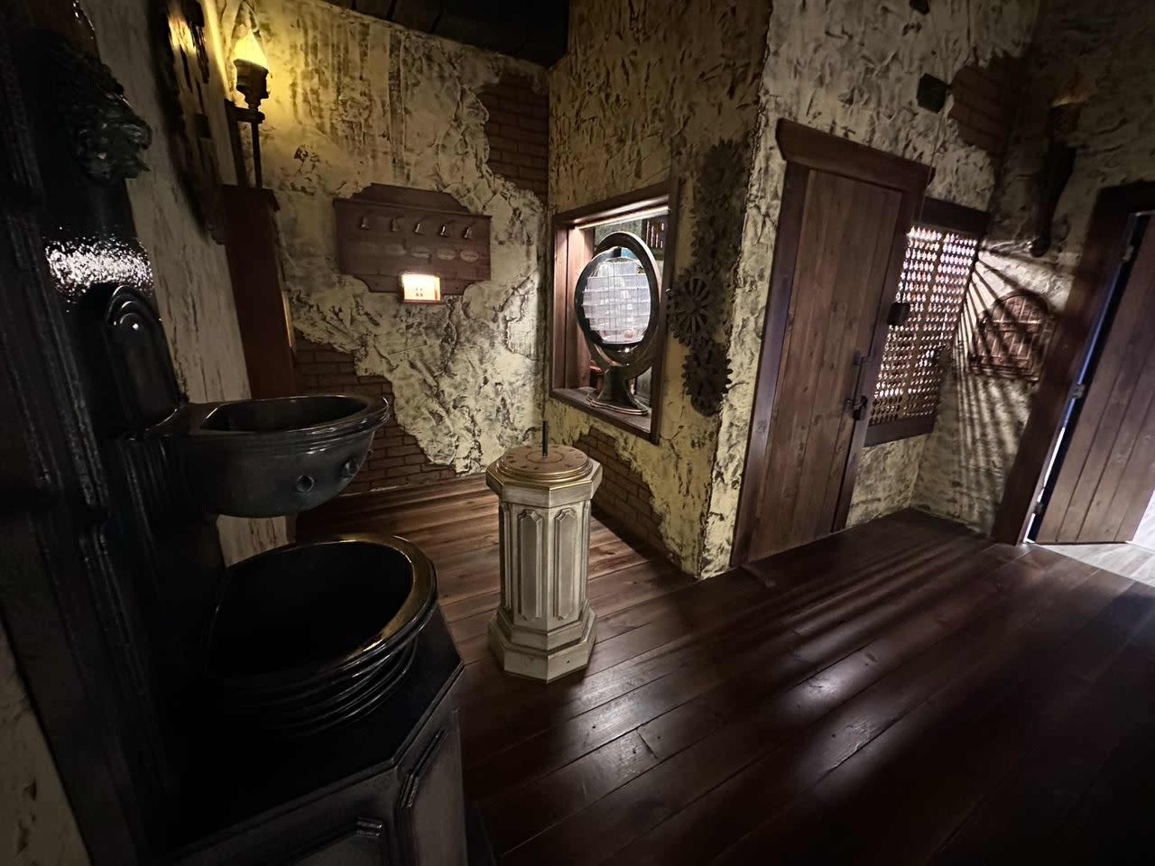 The image shows a dimly lit room with textured walls, wooden floors, and a decorative fountain beside a circular mirror, featuring a door and a small illuminated sign on the wall.