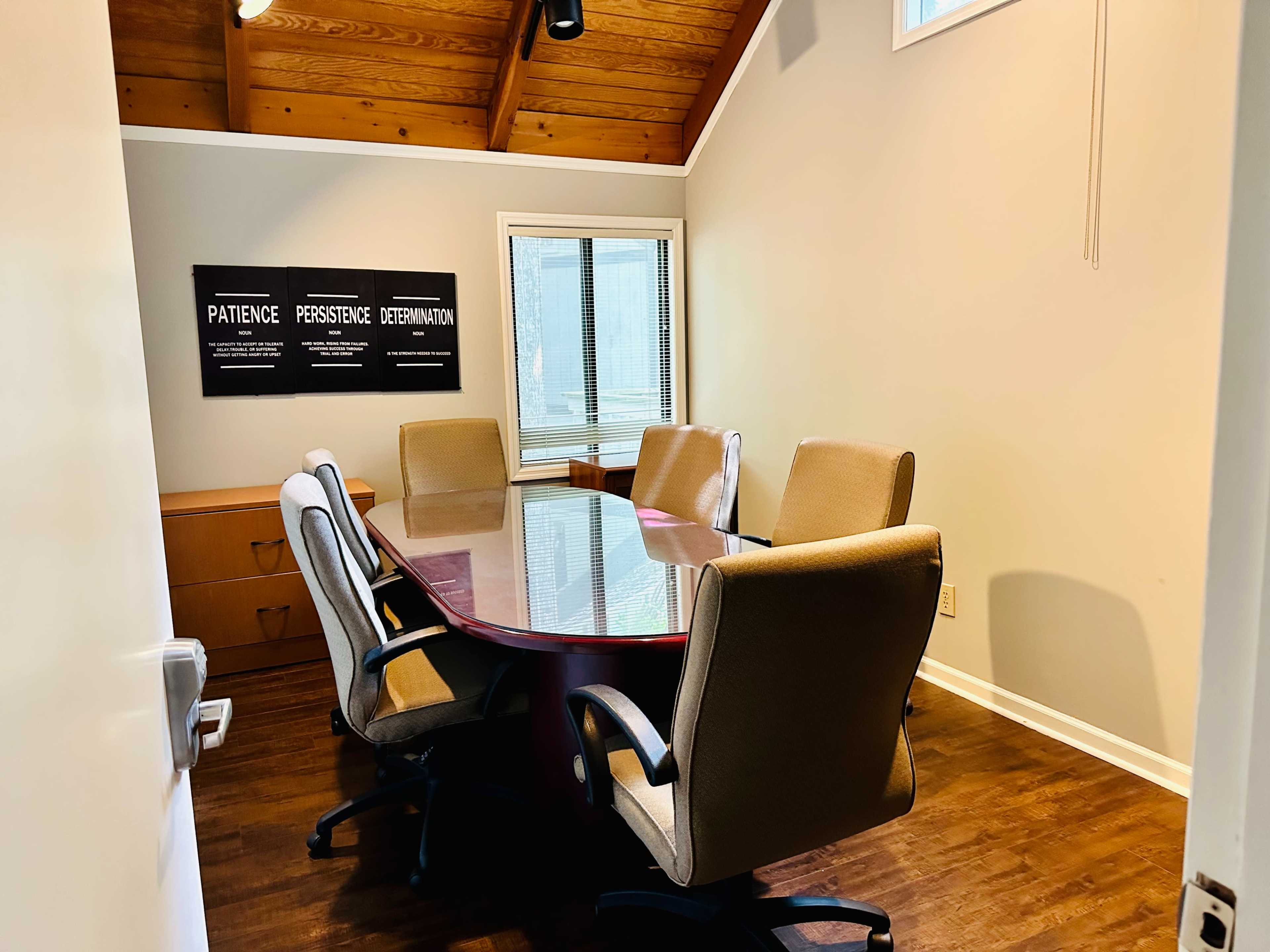 A conference room features a large oval table surrounded by six ergonomic chairs, with motivational posters on the wall.